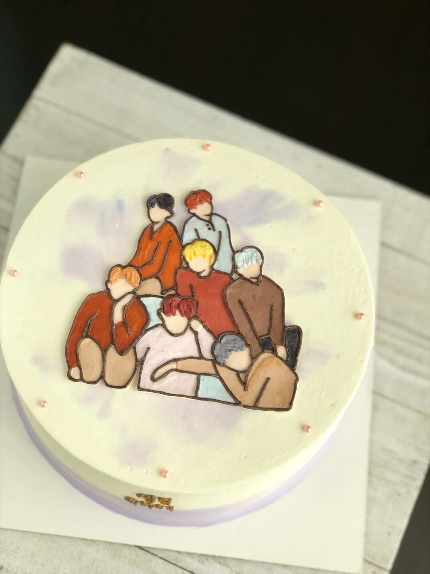 Round cake decorated with a drawing of several people gathered together, resting on a wooden board.
