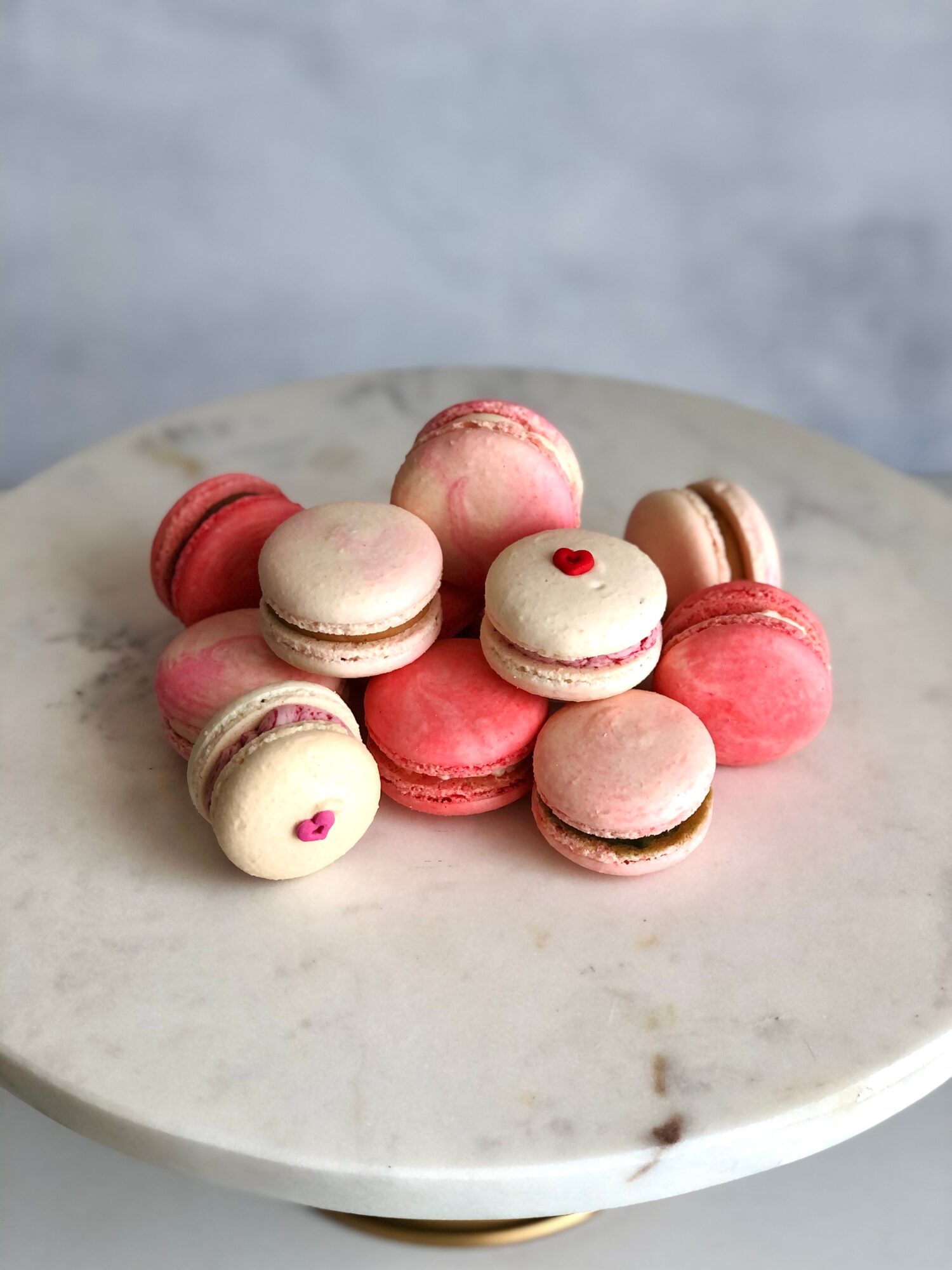 Pink, white, and brown macarons arranged on a round marble cake stand.