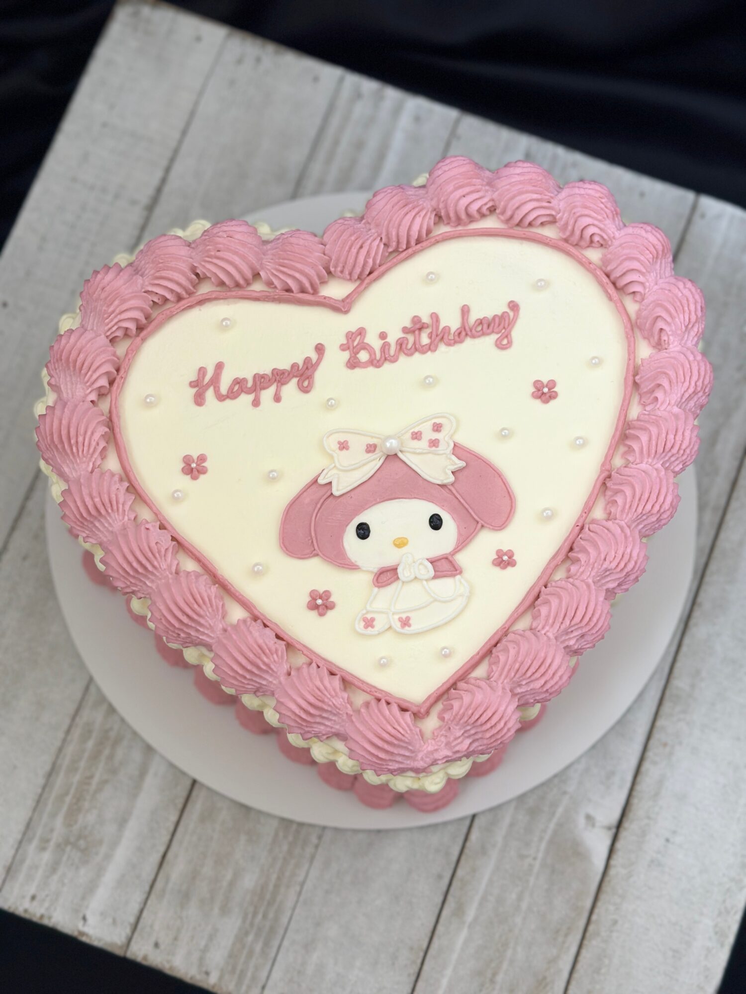 Heart-shaped pink cake with a white icing center, birthday message, and cartoon character decoration.