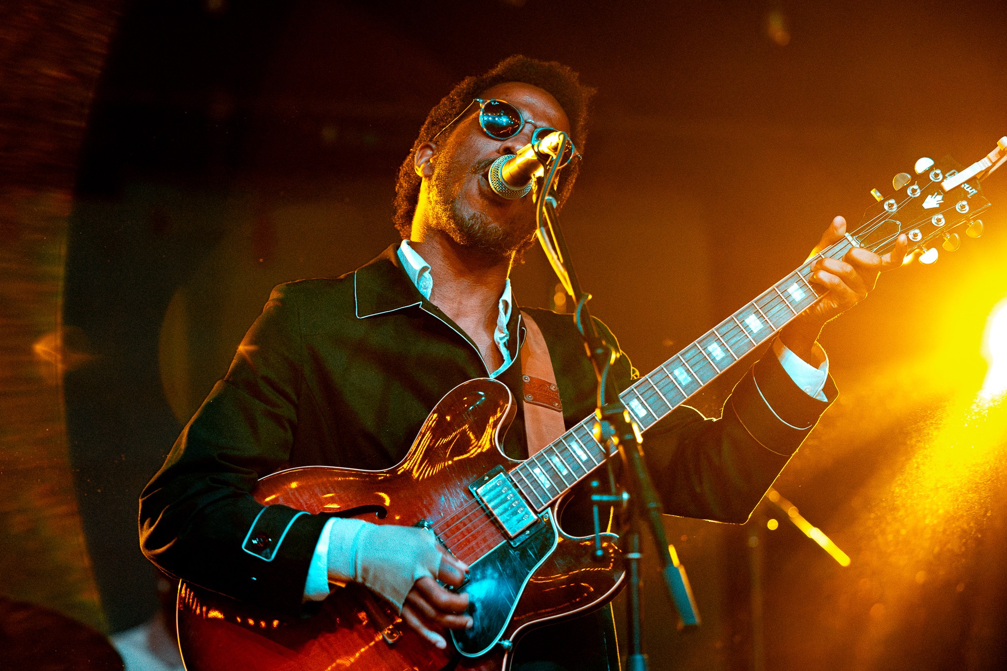 Musician with sunglasses playing an electric guitar on stage with warm lighting