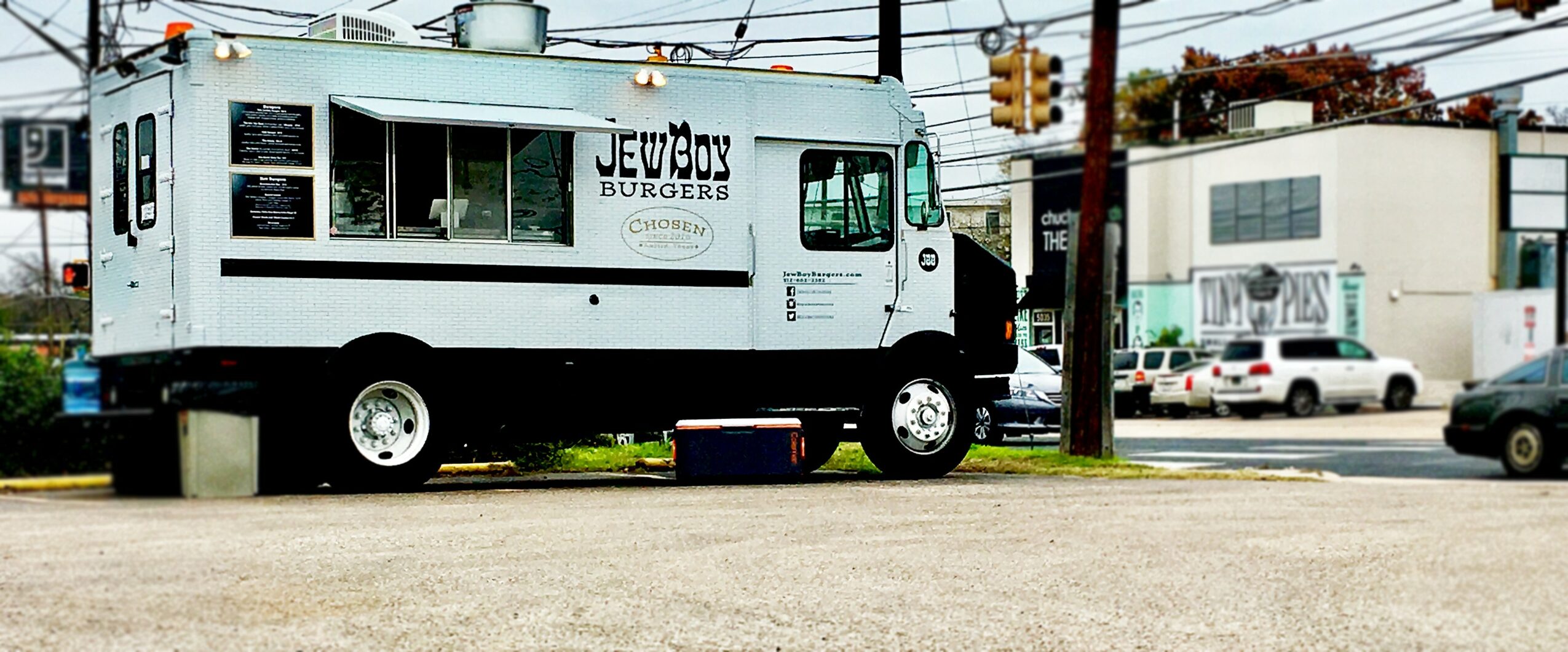 Food truck parked on street with buildings and cars in background.