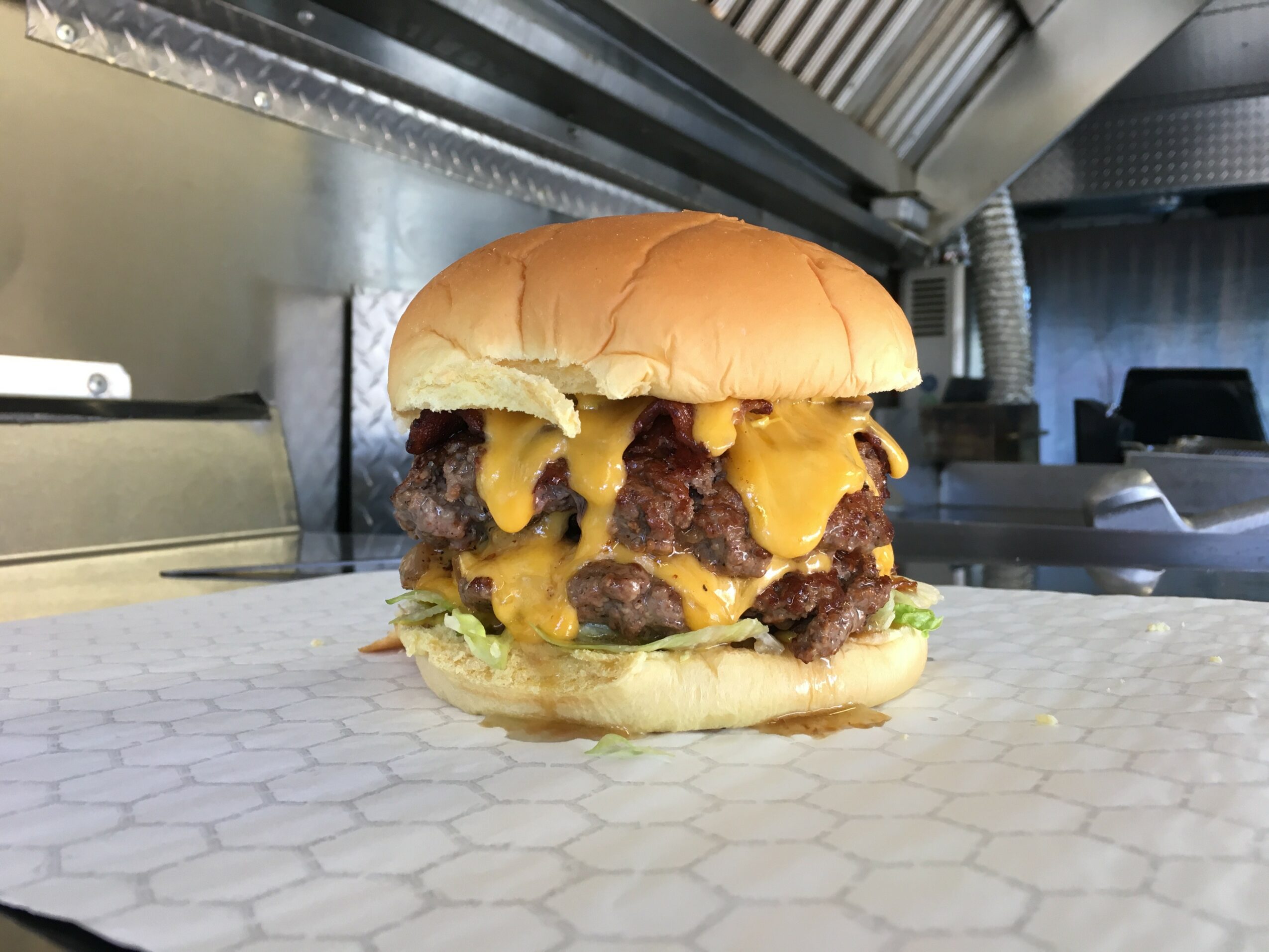 Cheeseburger with lettuce, cheese, and beef patty on a bun, placed on a paper sheet in a kitchen setting.