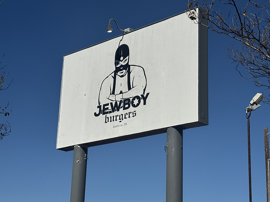 Billboard with a cartoon character wearing a mask and a hat, and the text 'JEWBOY burgers'.