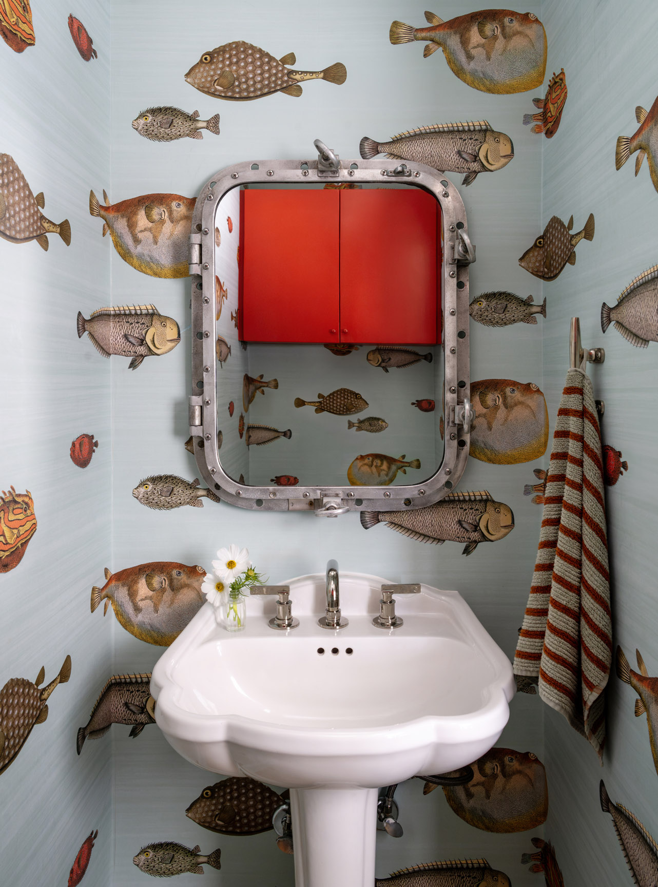 Bathroom with fish-themed wallpaper, mirror, sink, and striped towel, decorated with fish illustrations on the walls.