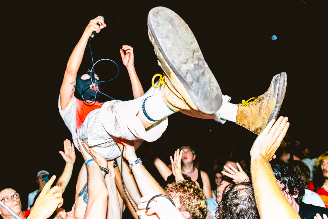 Person being lifted in the air during a concert or event, with hands reaching up around them, dark background.