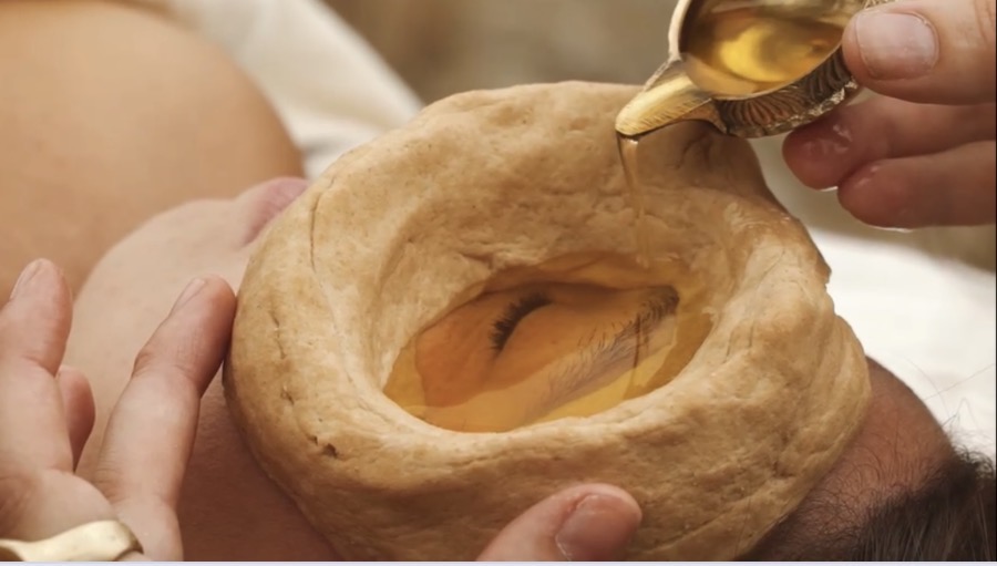 Person's mouth open with a large bread bowl filled with honey being poured into it, hands holding the bread.