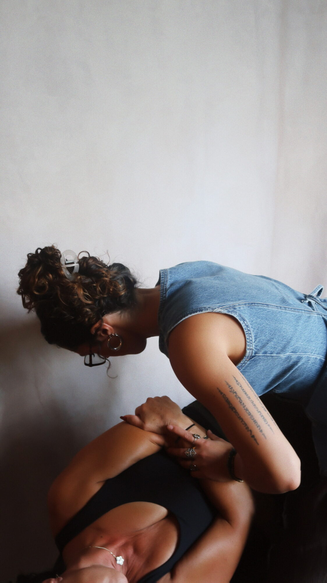 Two people lying on the floor, one with curly hair in a bun, the other with short hair, holding hands.