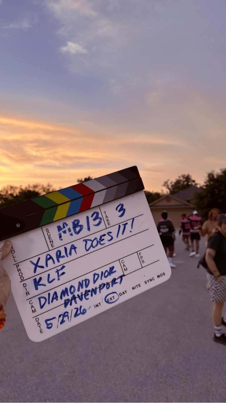 People gathered outdoors during sunset, with a colorful sky and trees in the background.