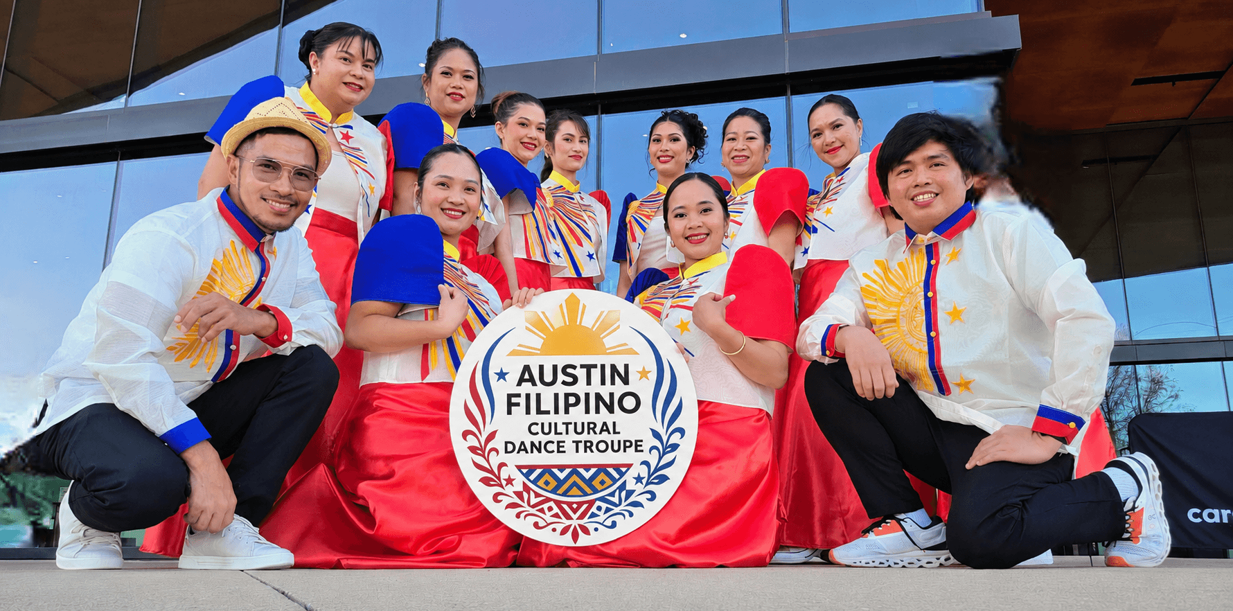 Group of people in traditional Filipino costumes holding a sign that says 'Austin Filipino Cultural Dance Troupe'.
