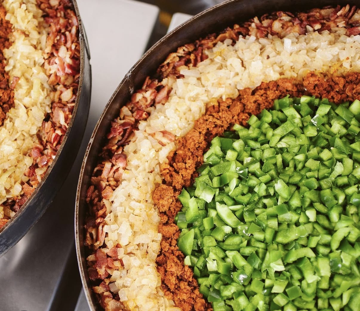 Close-up of a layered dish with chopped green vegetables, ground meat, rice, and other ingredients in a round pan.
