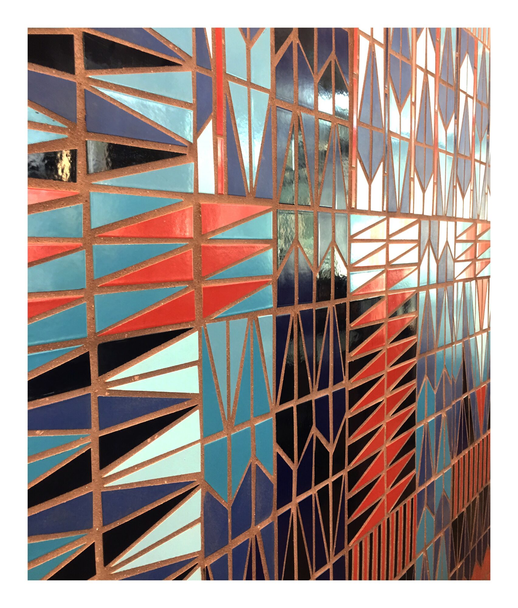 Close-up of a colorful geometric patterned wall with triangular and rectangular shapes in blue, red, black, and brown.
