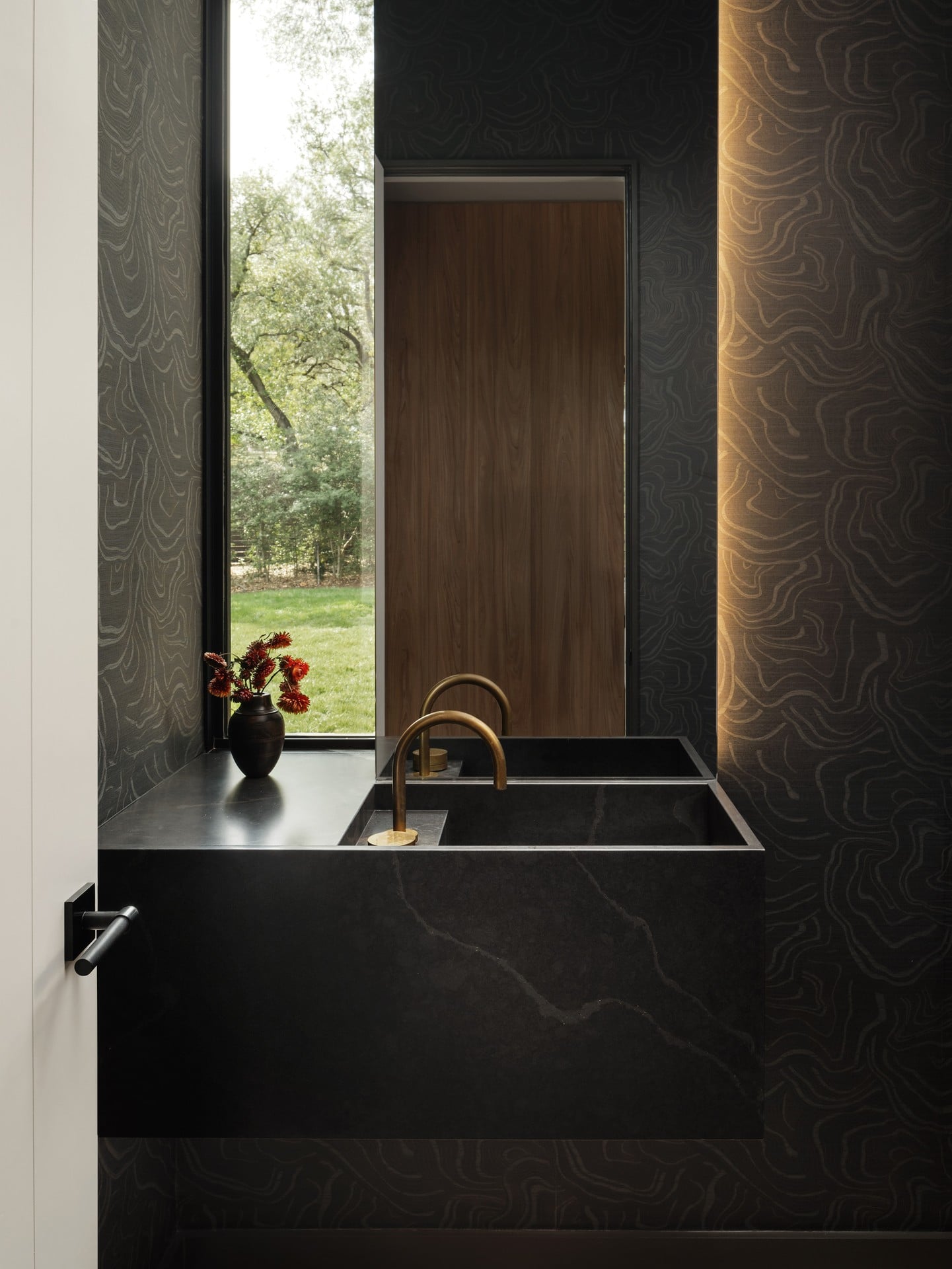 Interior with a black marble sink, gold faucet, and a window showing trees outside.