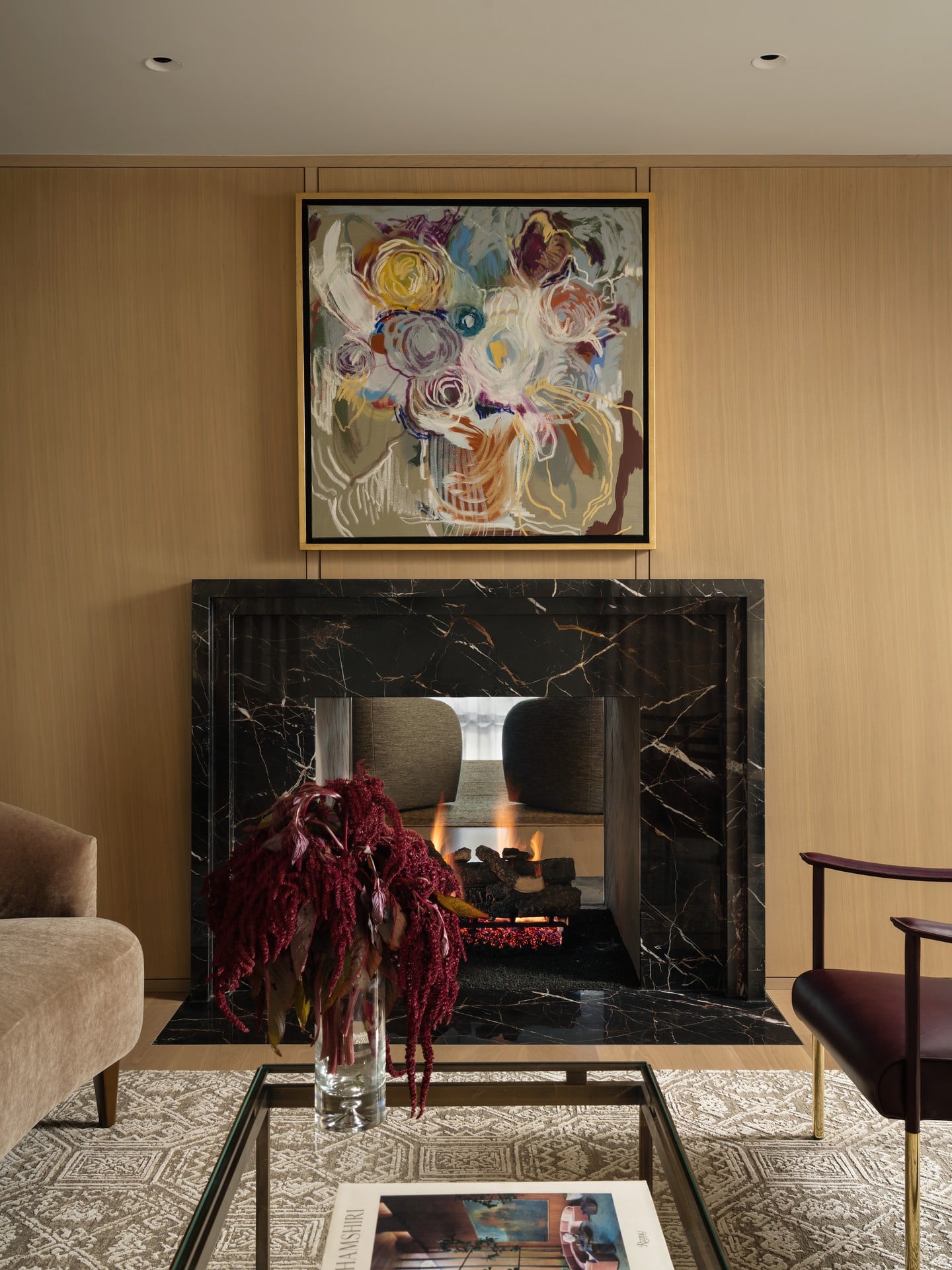 Living room with a black marble fireplace, abstract painting above, and a glass table with a red floral arrangement.