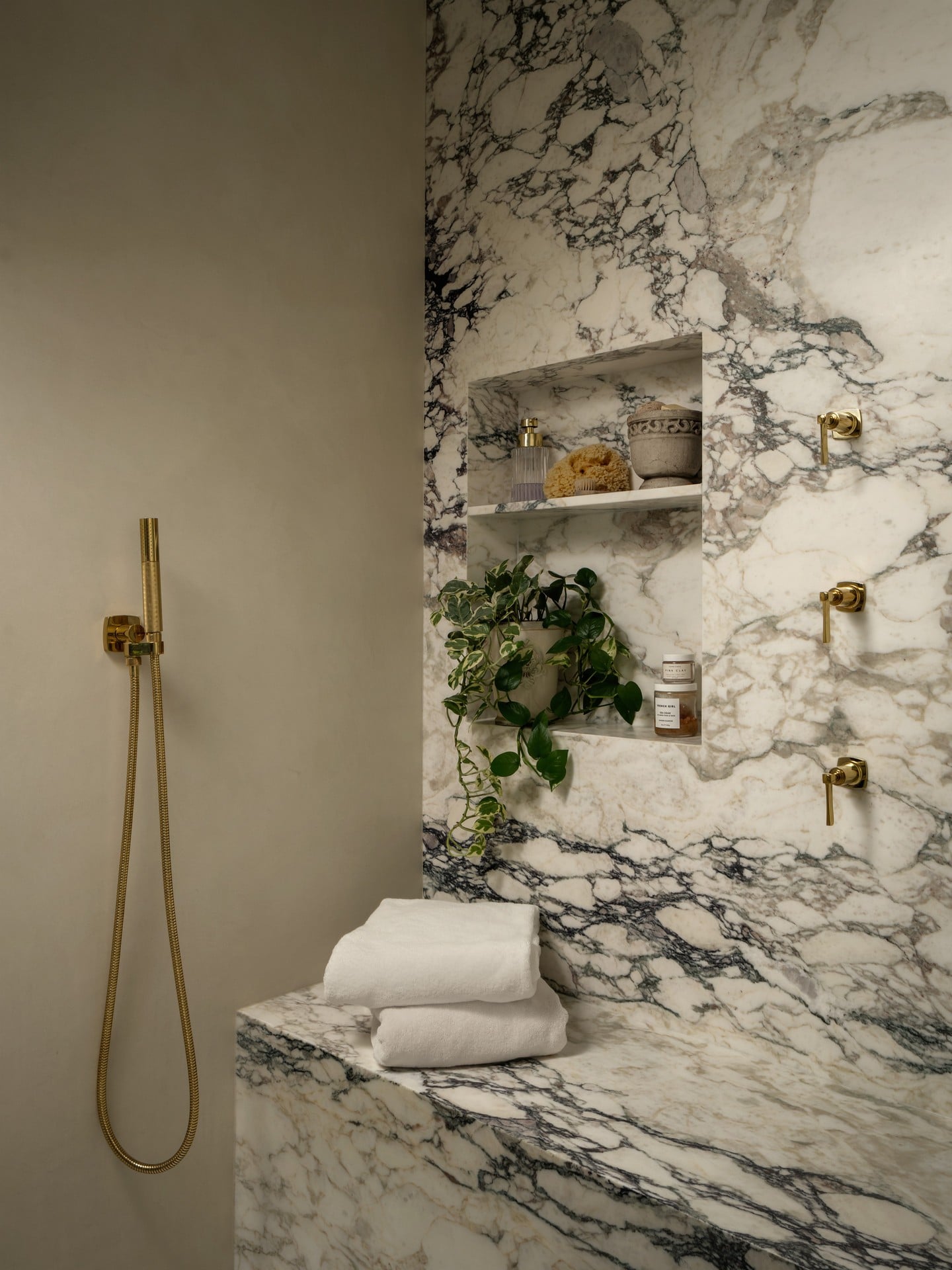 Bathroom with marble wall and countertop, shelves with decor, towels, and a shower hose on the left.