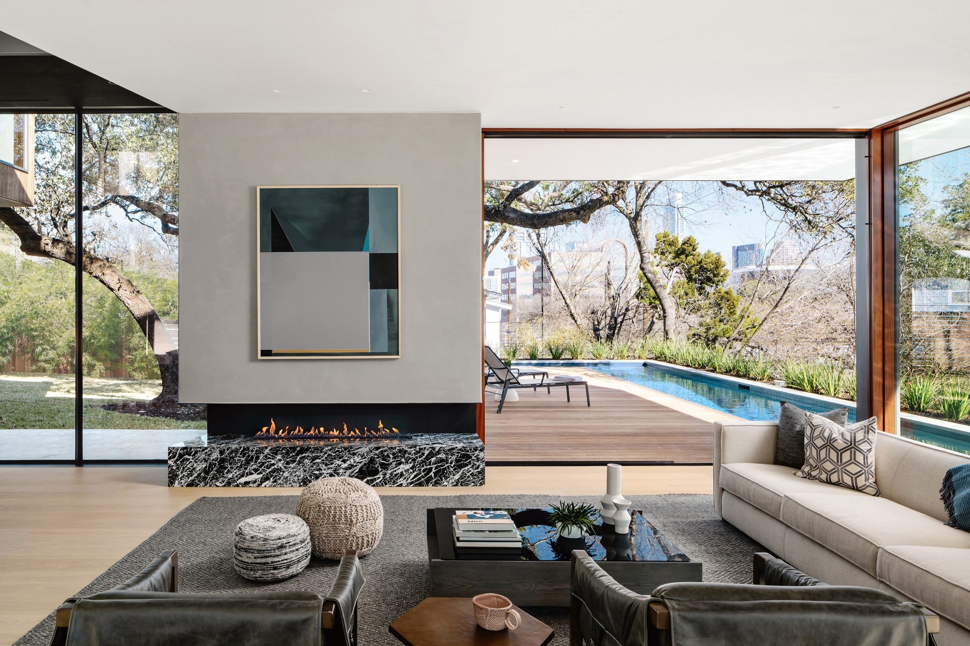 Living room with large windows, fireplace, sofa, and view of outdoor pool and trees.