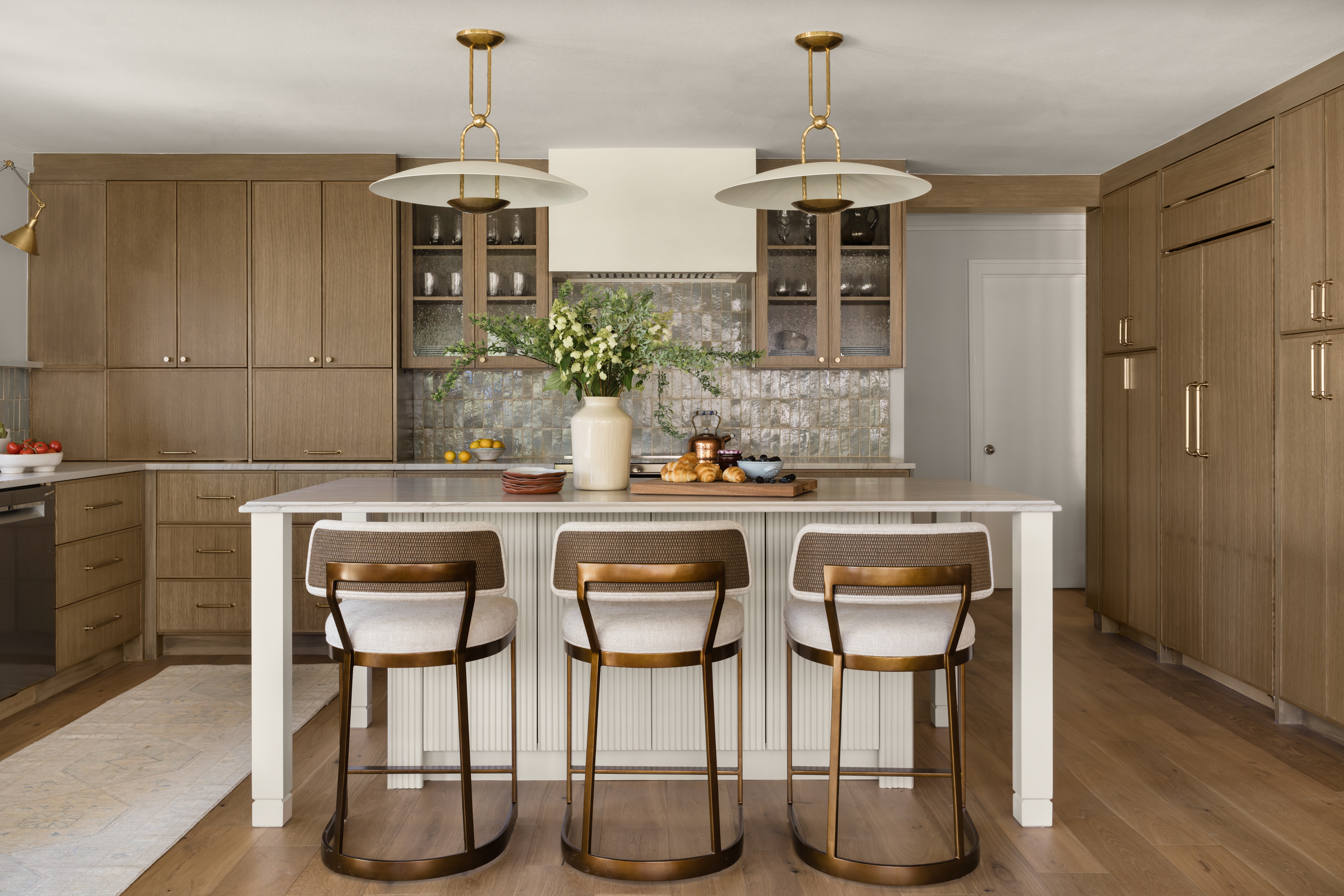 Bright kitchen with wood cabinetry, a central island, three stools, pendant lights, and flowers on the counter.