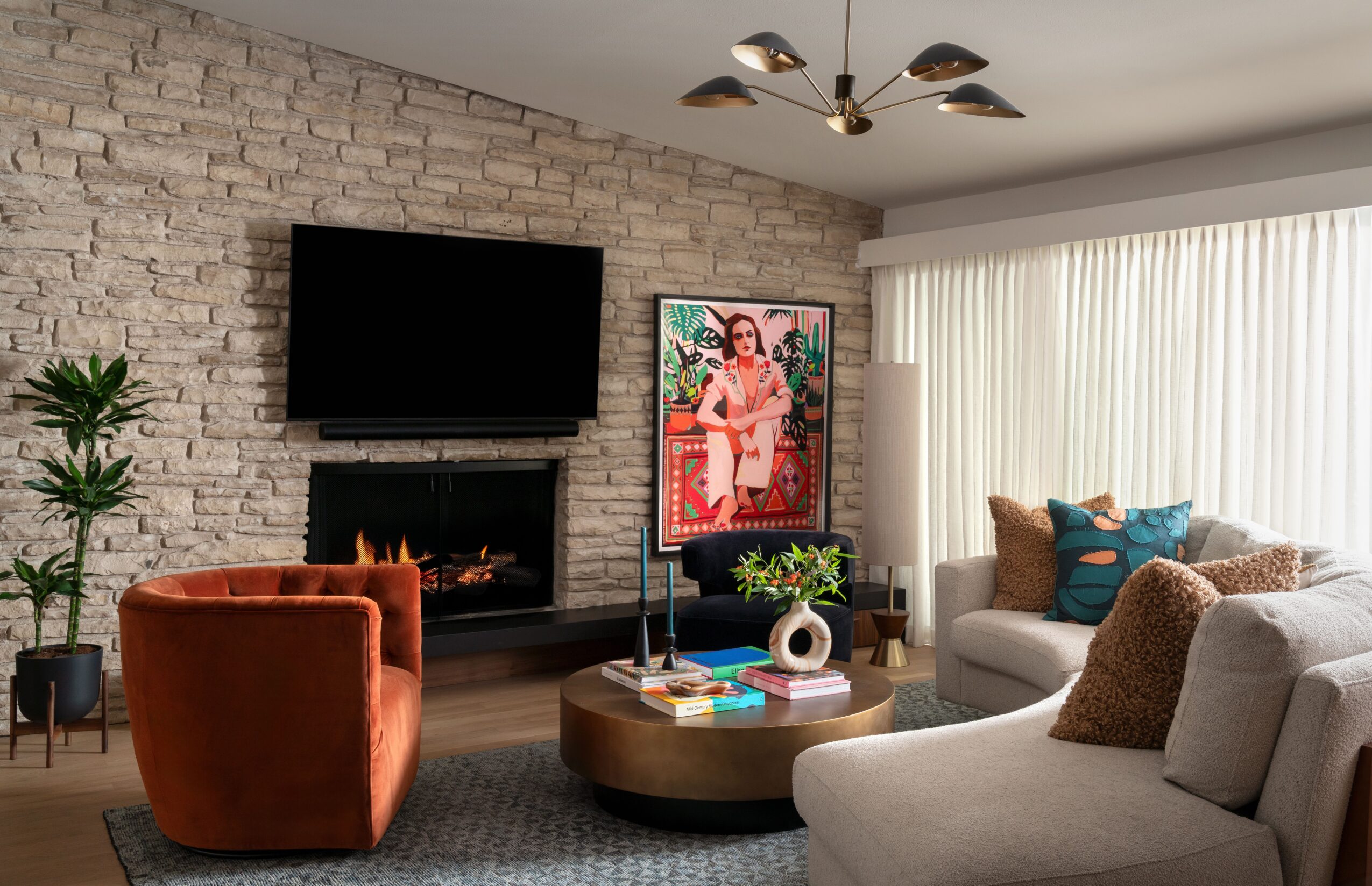 Living room with a stone wall, television, fireplace, seating, coffee table, and tall windows with curtains.