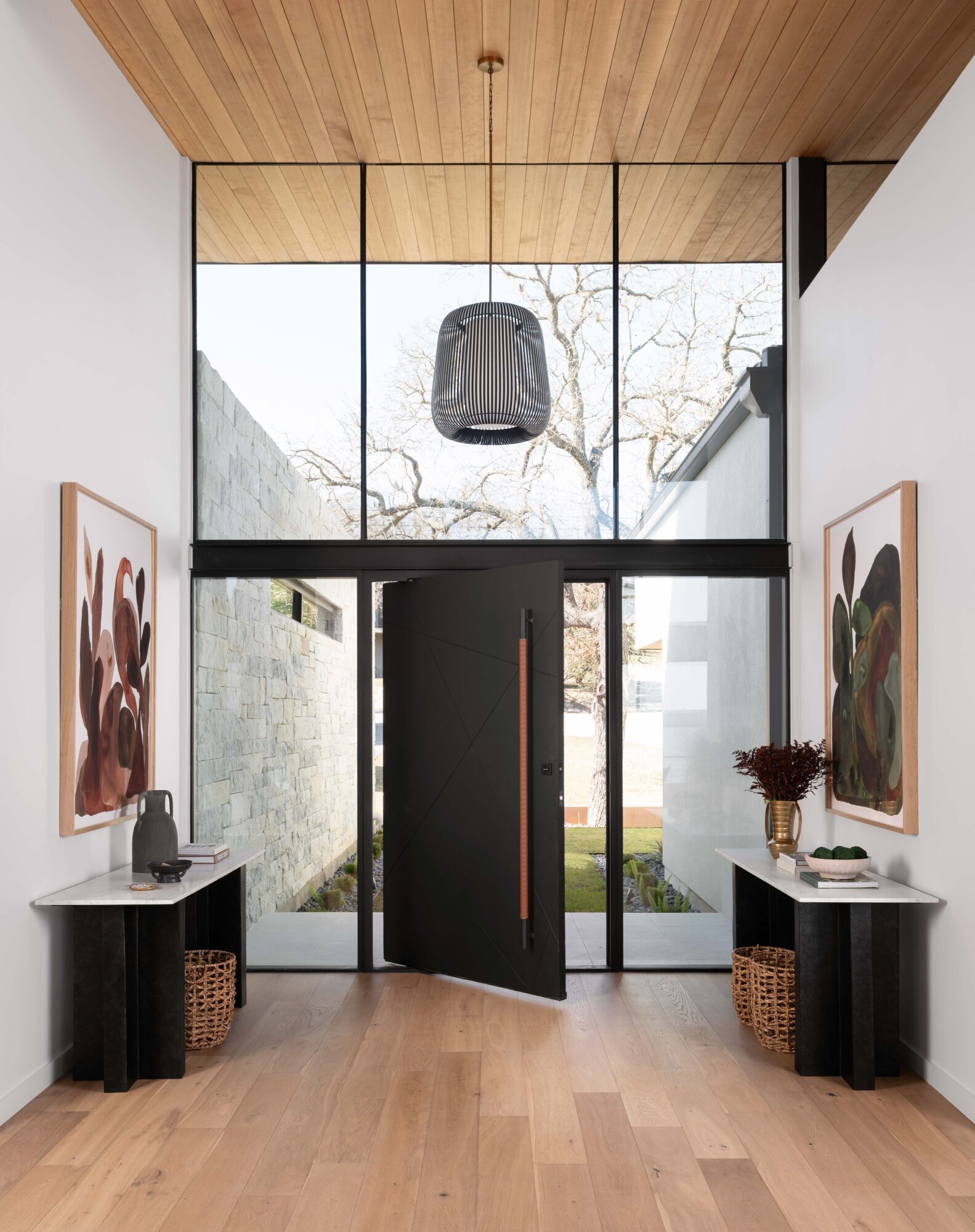 Modern entryway with a wood ceiling, glass doors, framed artwork, and a hanging light fixture.