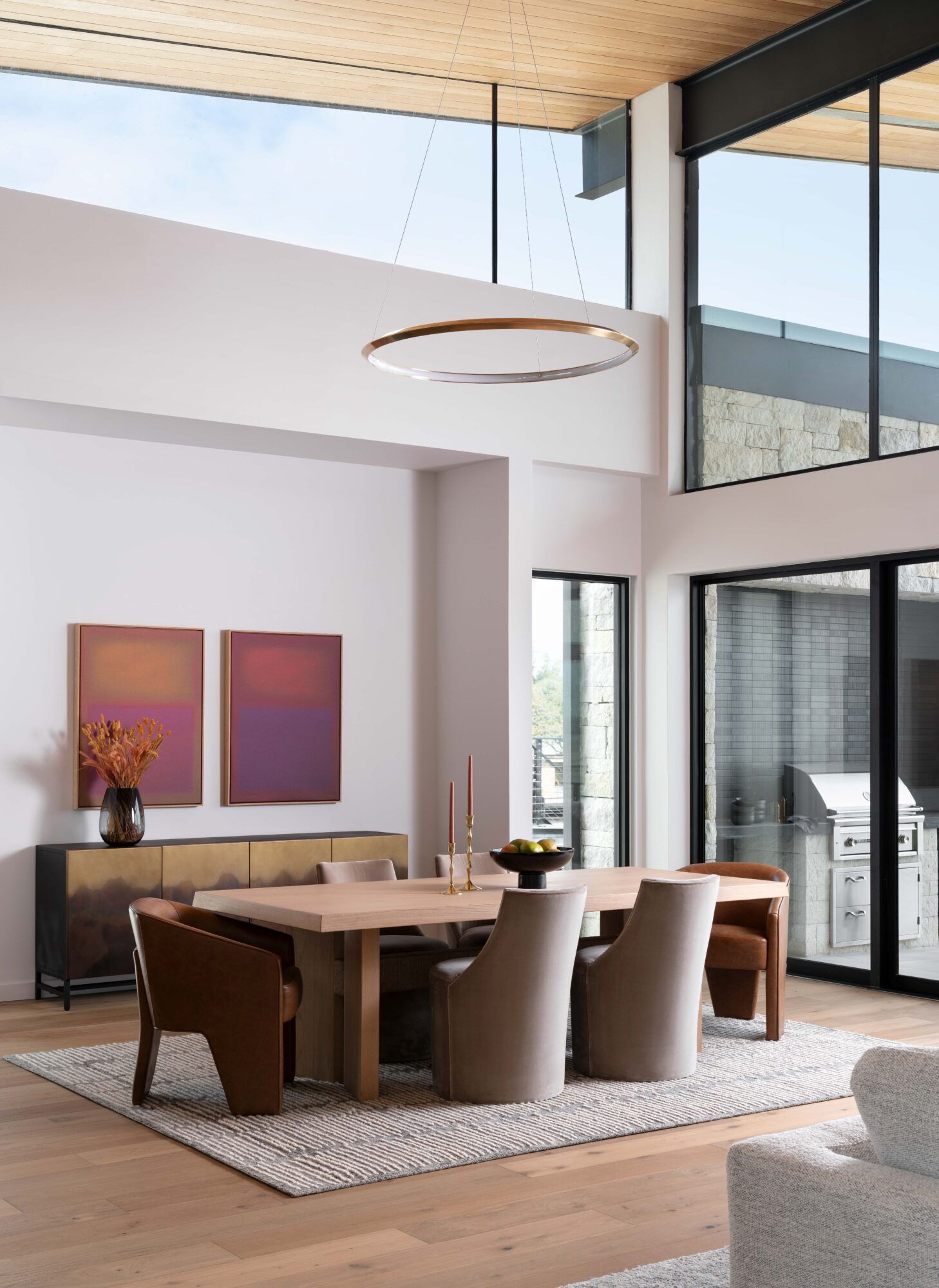 Modern dining area with a wooden table, upholstered chairs, pendant light, large windows, and framed wall art.