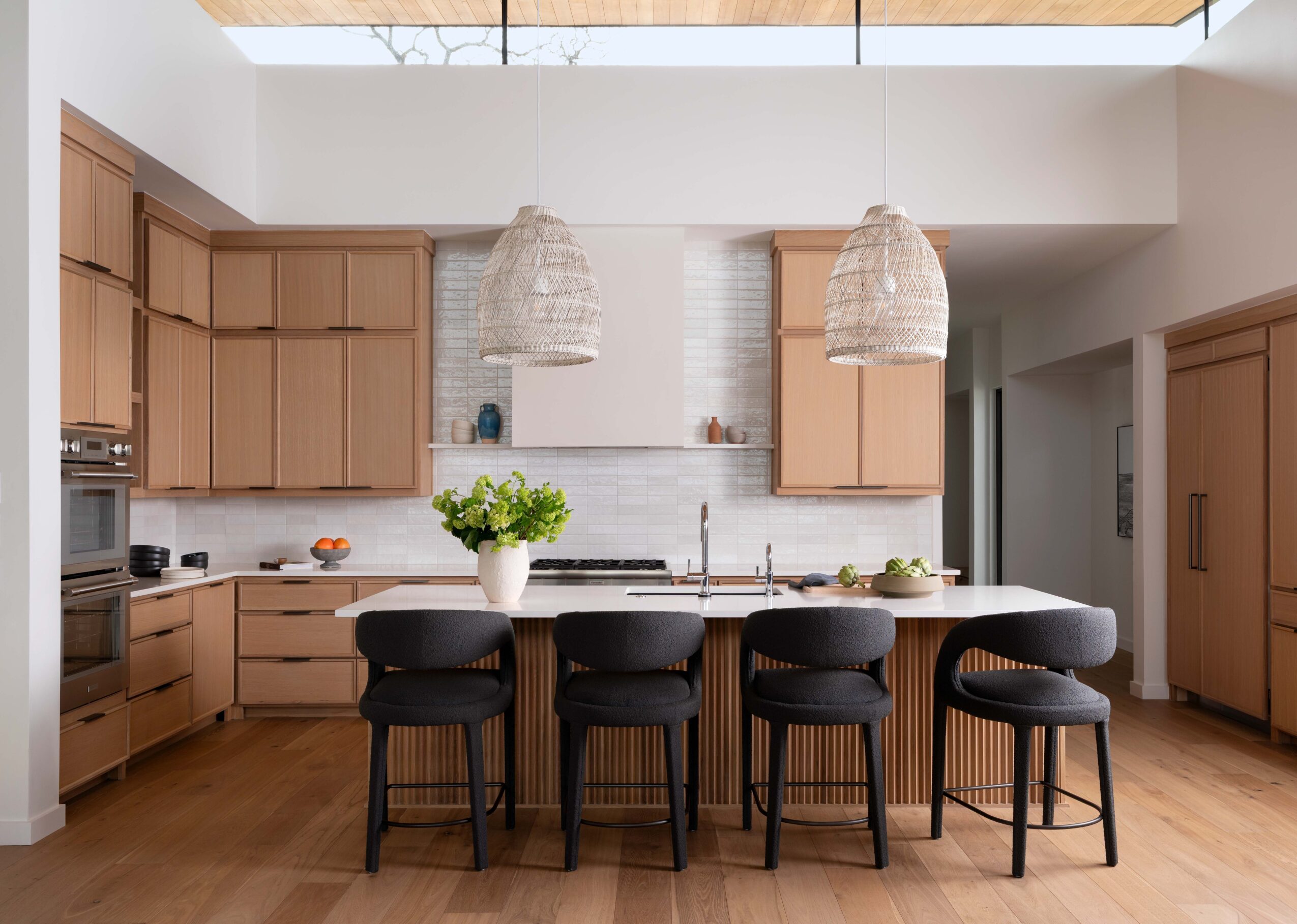 Modern kitchen with a long island, four stools, wooden cabinets, pendant lights, and a skylight.
