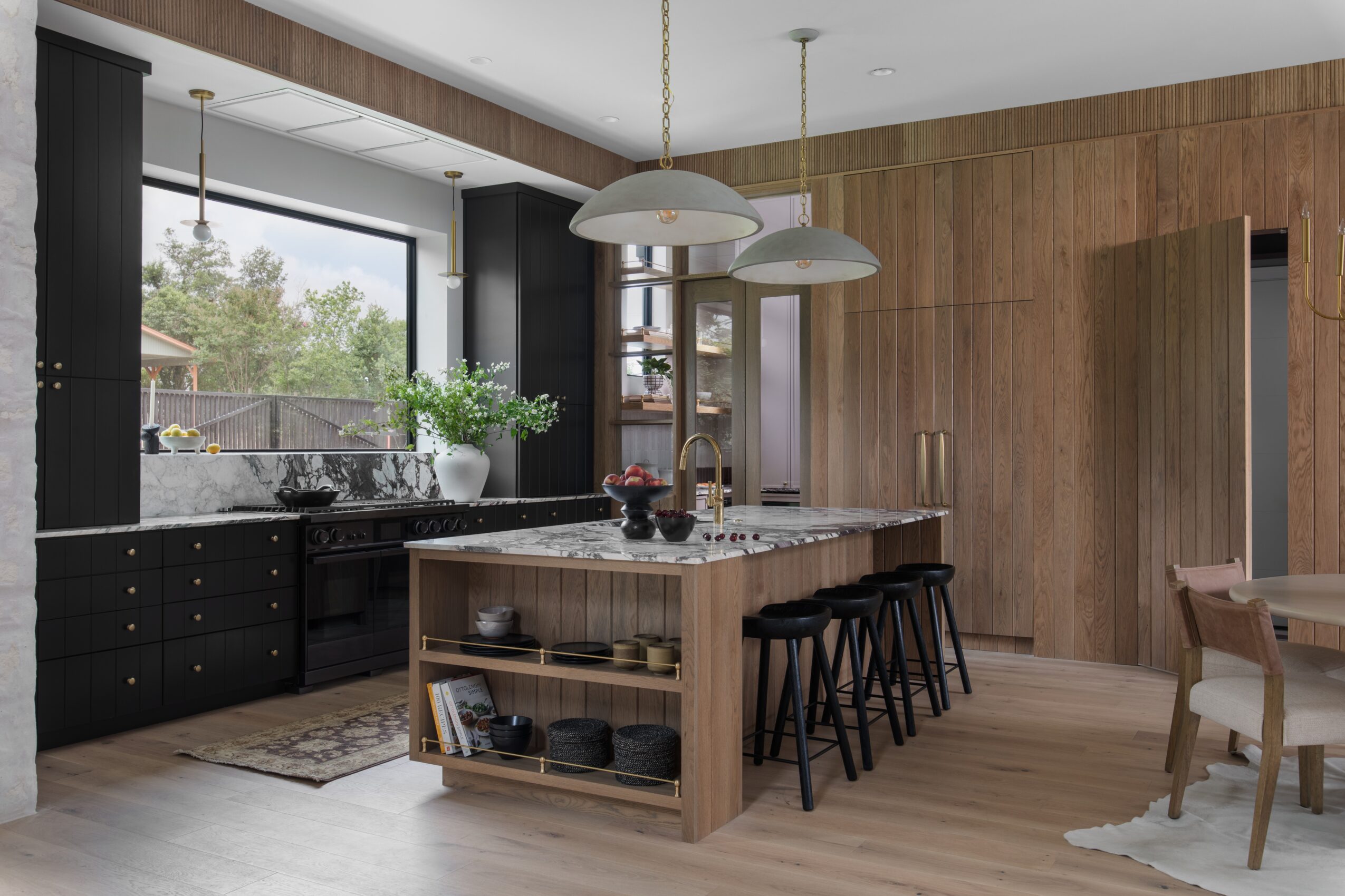 Modern kitchen with a wood-paneled island, black cabinets, pendant lights, and a dining table.