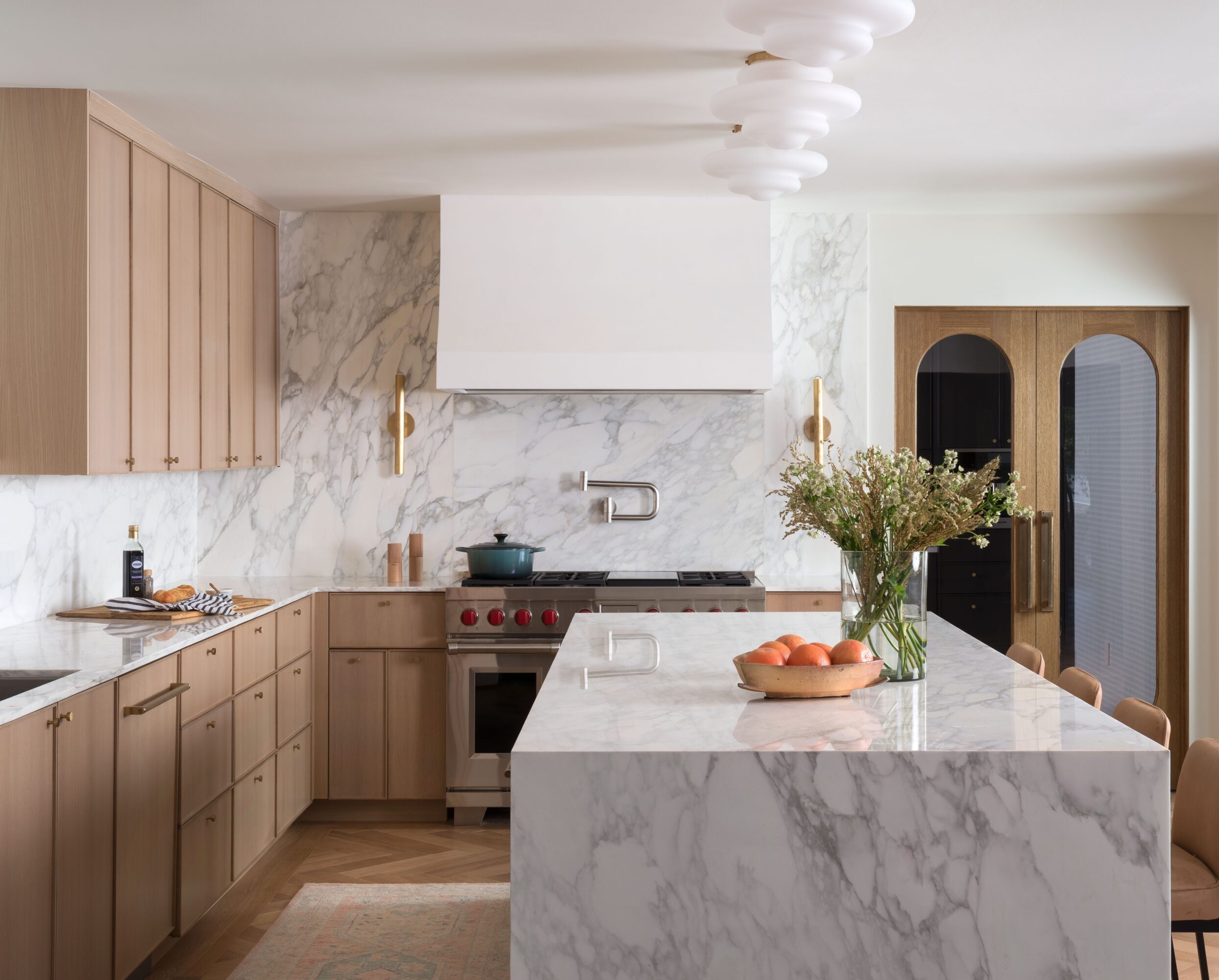 Bright kitchen with marble countertops, wood cabinetry, a cooking range, island, and a vase of flowers.