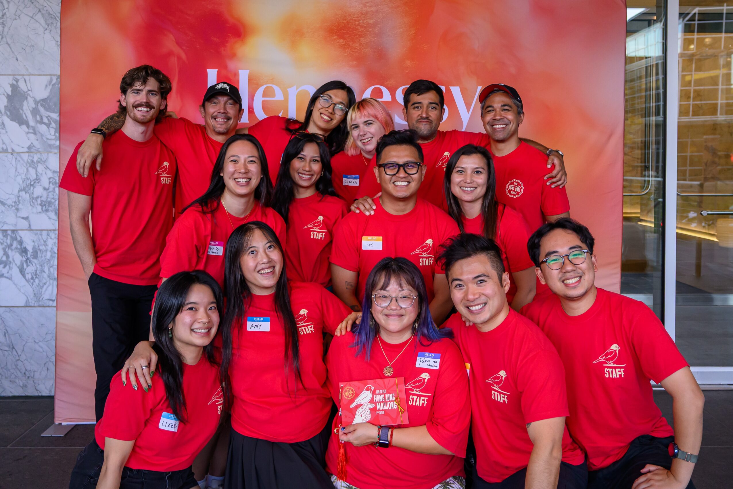 Group of people wearing red shirts pose together in front of a red backdrop.
