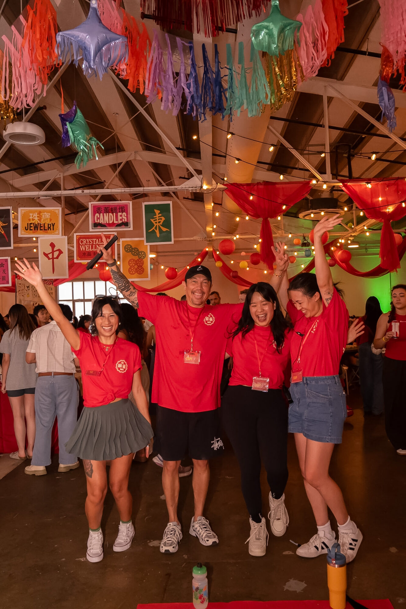 People pose beneath colorful hanging decorations and string lights in a festive indoor space.