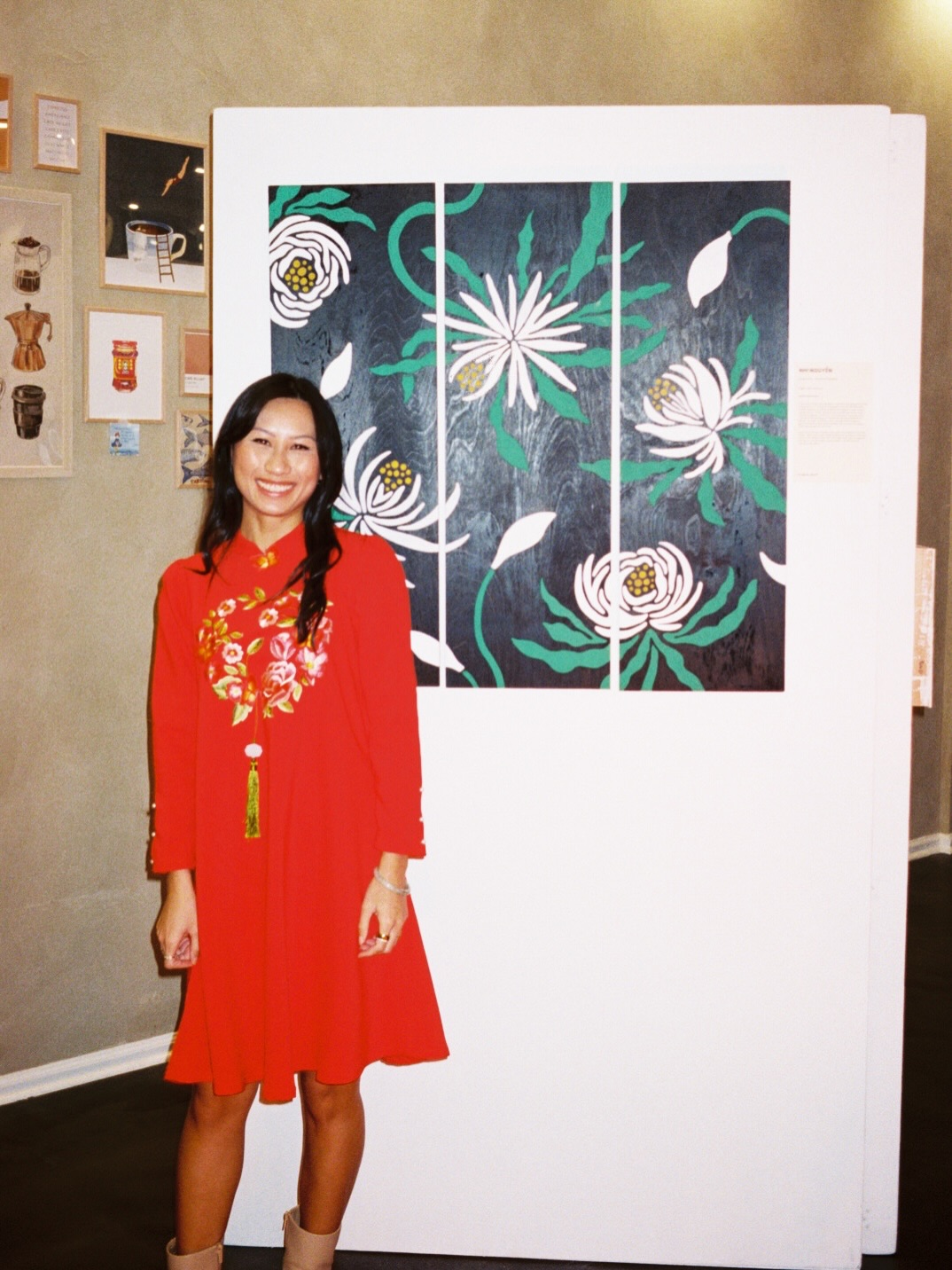 Person in a red dress standing beside a large floral artwork displayed on a white panel.