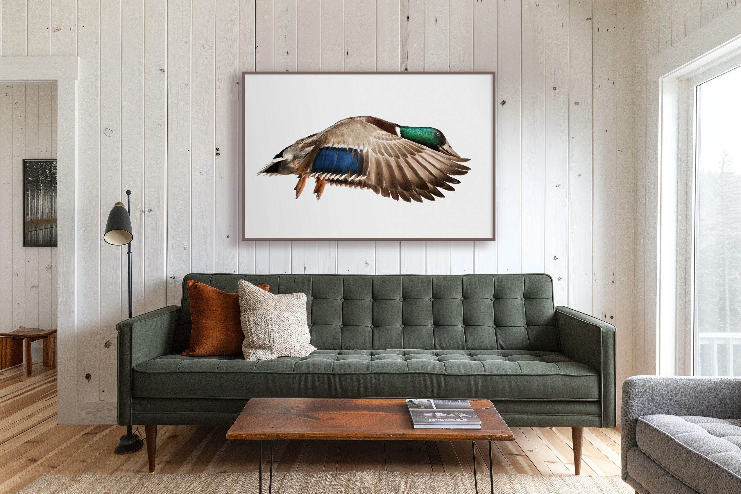 A framed illustration of a flying duck hangs above a dark green sofa in a bright living room.