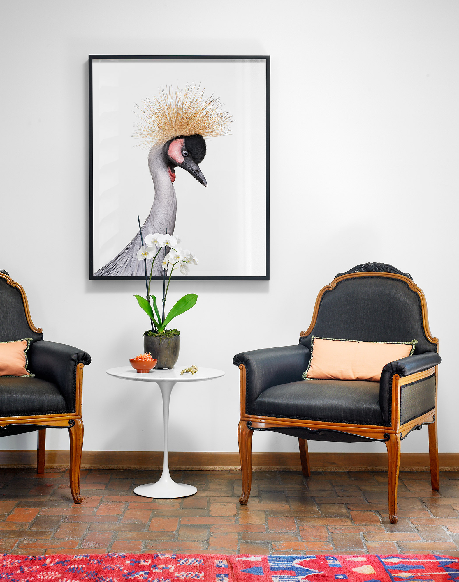 Two black armchairs flank a small white table beneath framed artwork of a crowned crane.