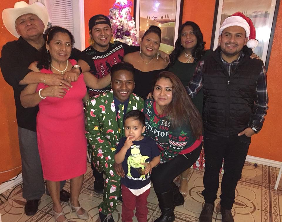 Group of people posing together indoors in front of decorated walls and a small Christmas tree.