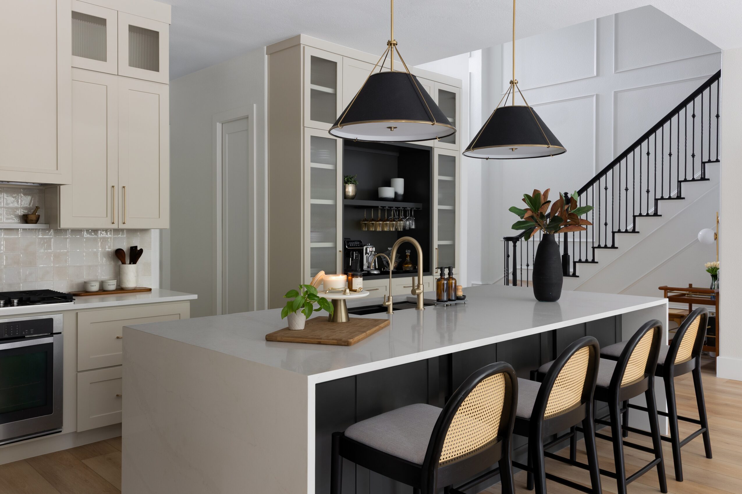 Bright kitchen with a large island, pendant lights, bar stools, and a staircase along the right wall.