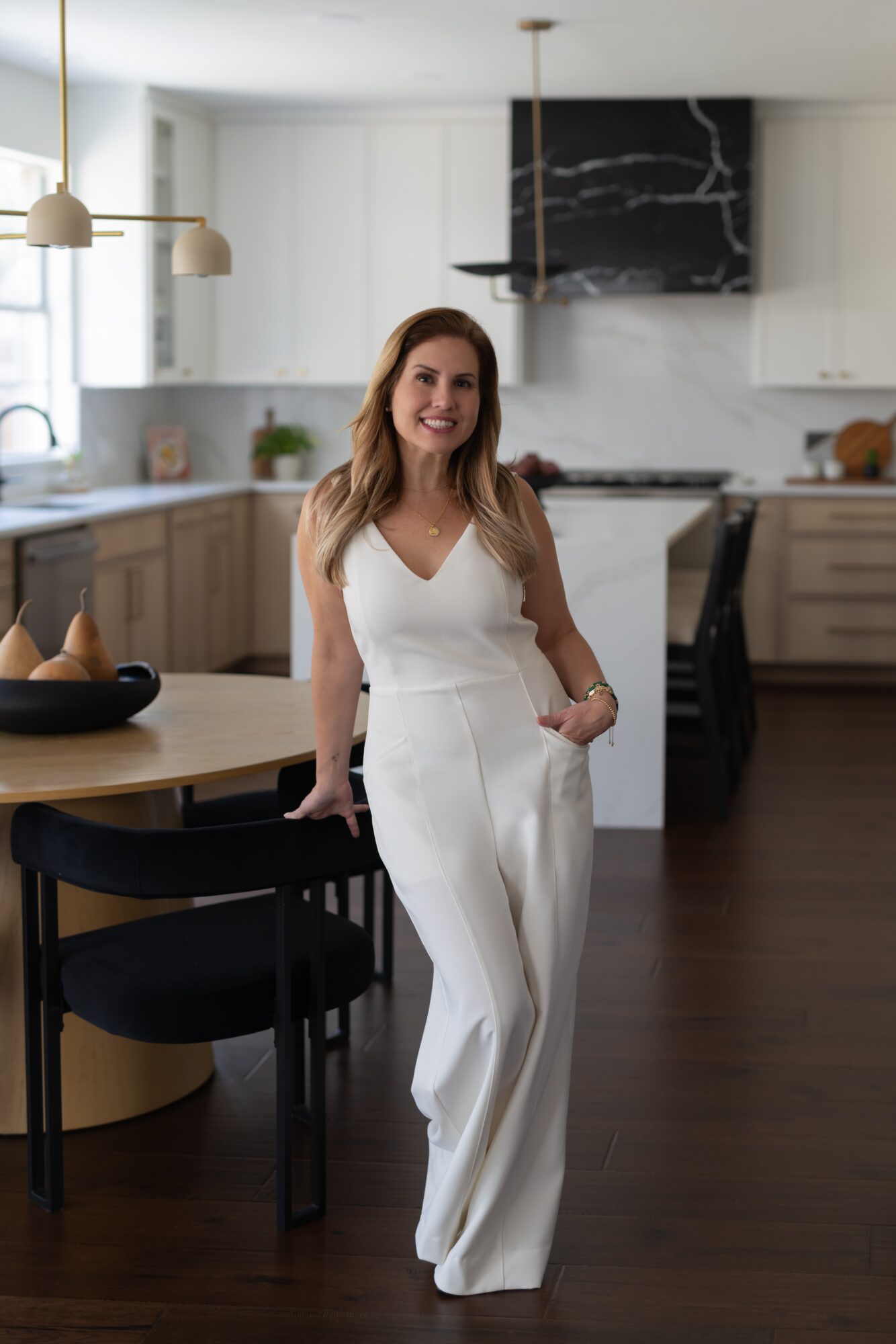 A person in a white outfit stands beside a dining table in a modern kitchen.