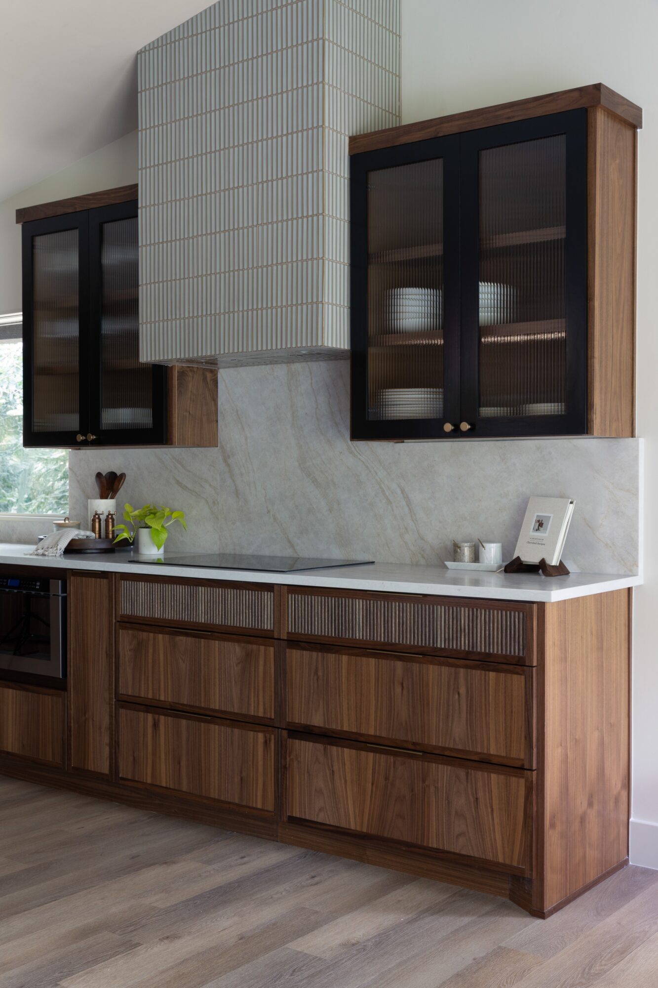Modern kitchen with wood cabinets, a marble backsplash, dark glass-front upper cabinets, and a central tiled range hood.