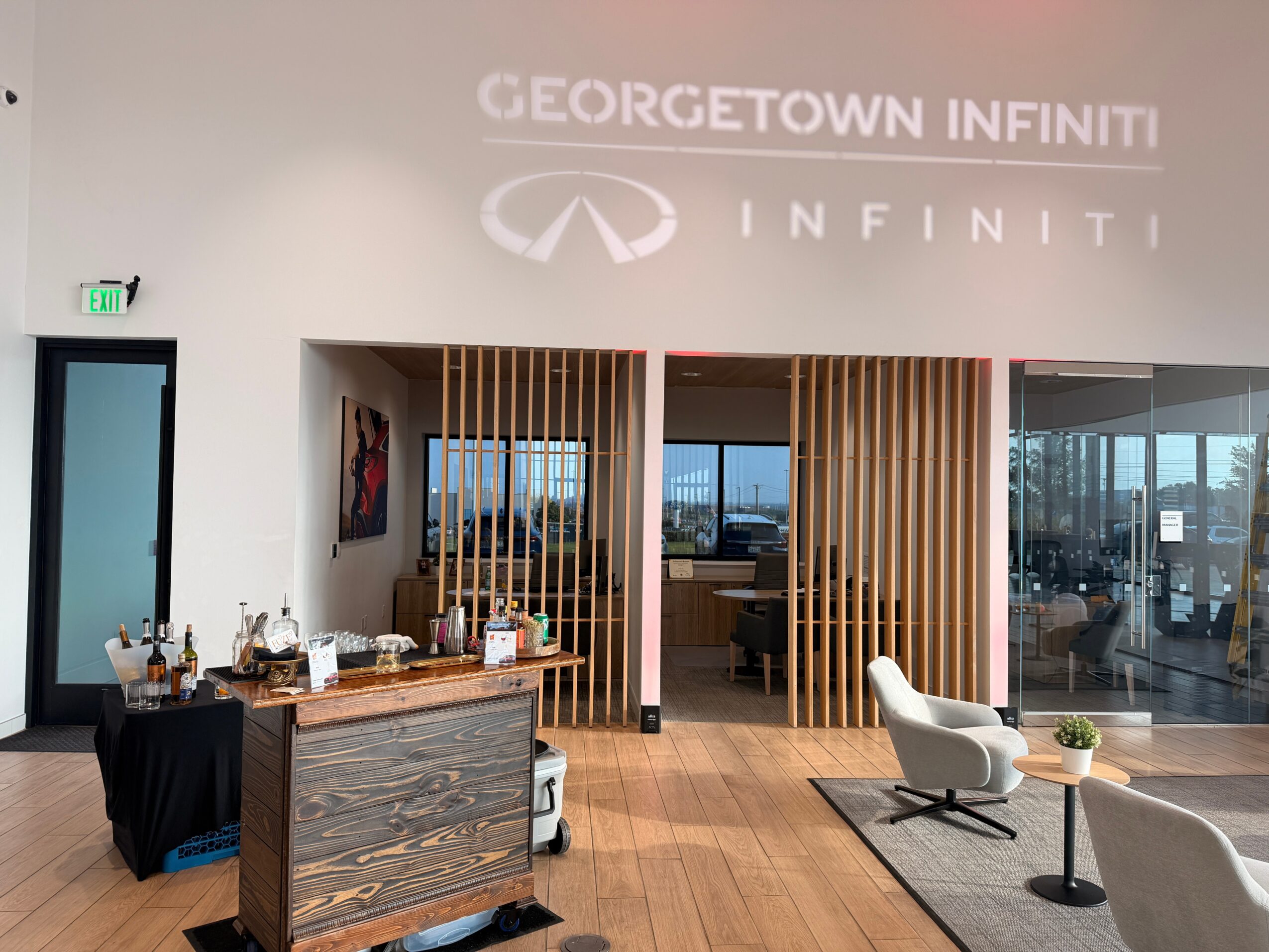 Modern Infiniti showroom with a reception desk, wood-slat partitions, glass doors, and lounge chairs.