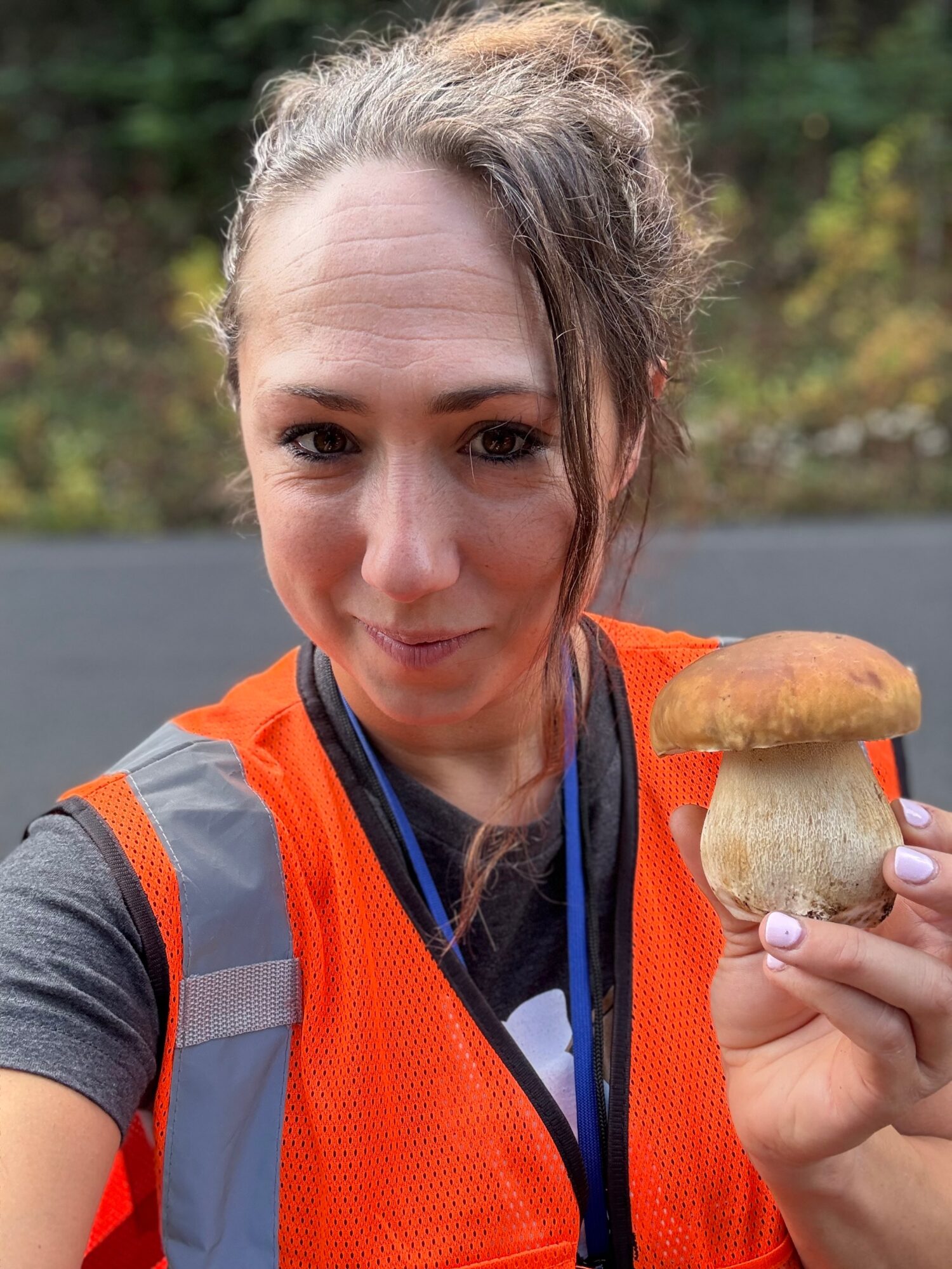 Person wearing an orange safety vest holds a mushroom outdoors.
