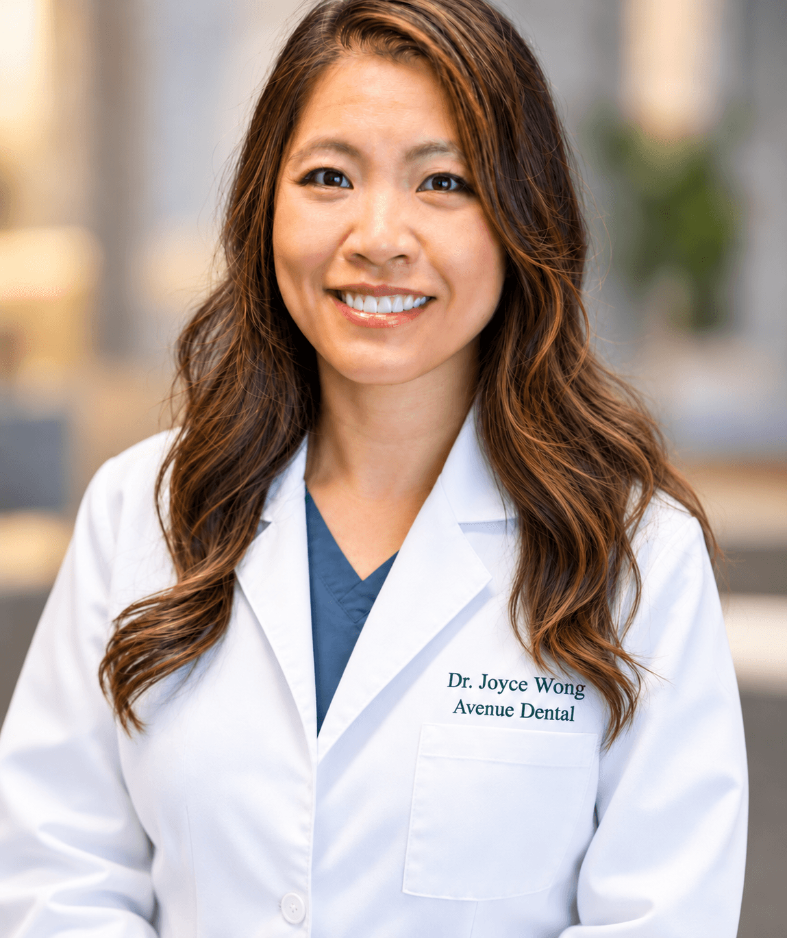 Smiling person wearing a white coat embroidered with “Dr. Joyce Wong, Avenue Dental.”