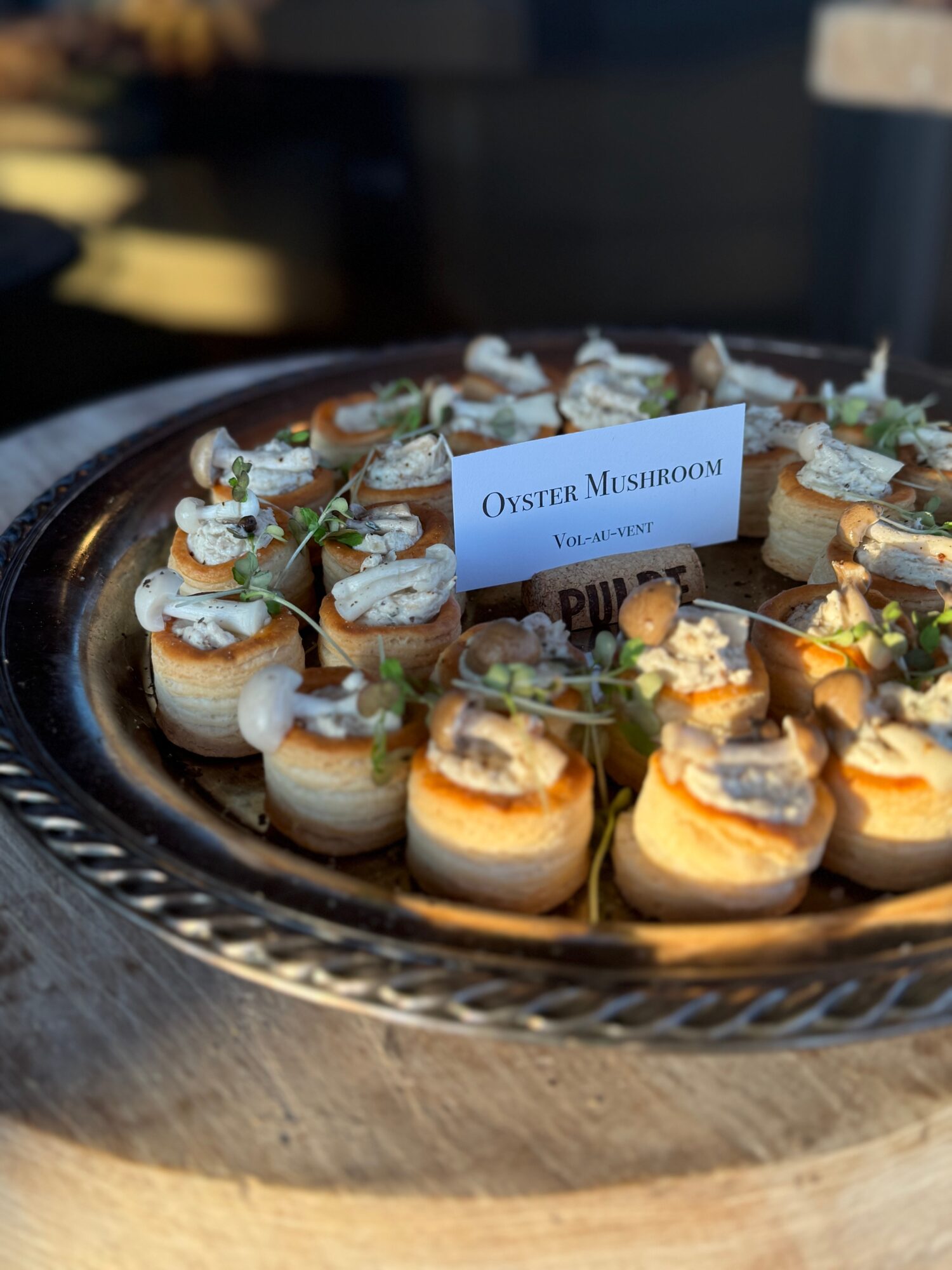 A platter of stuffed oyster mushrooms arranged around a small label card.