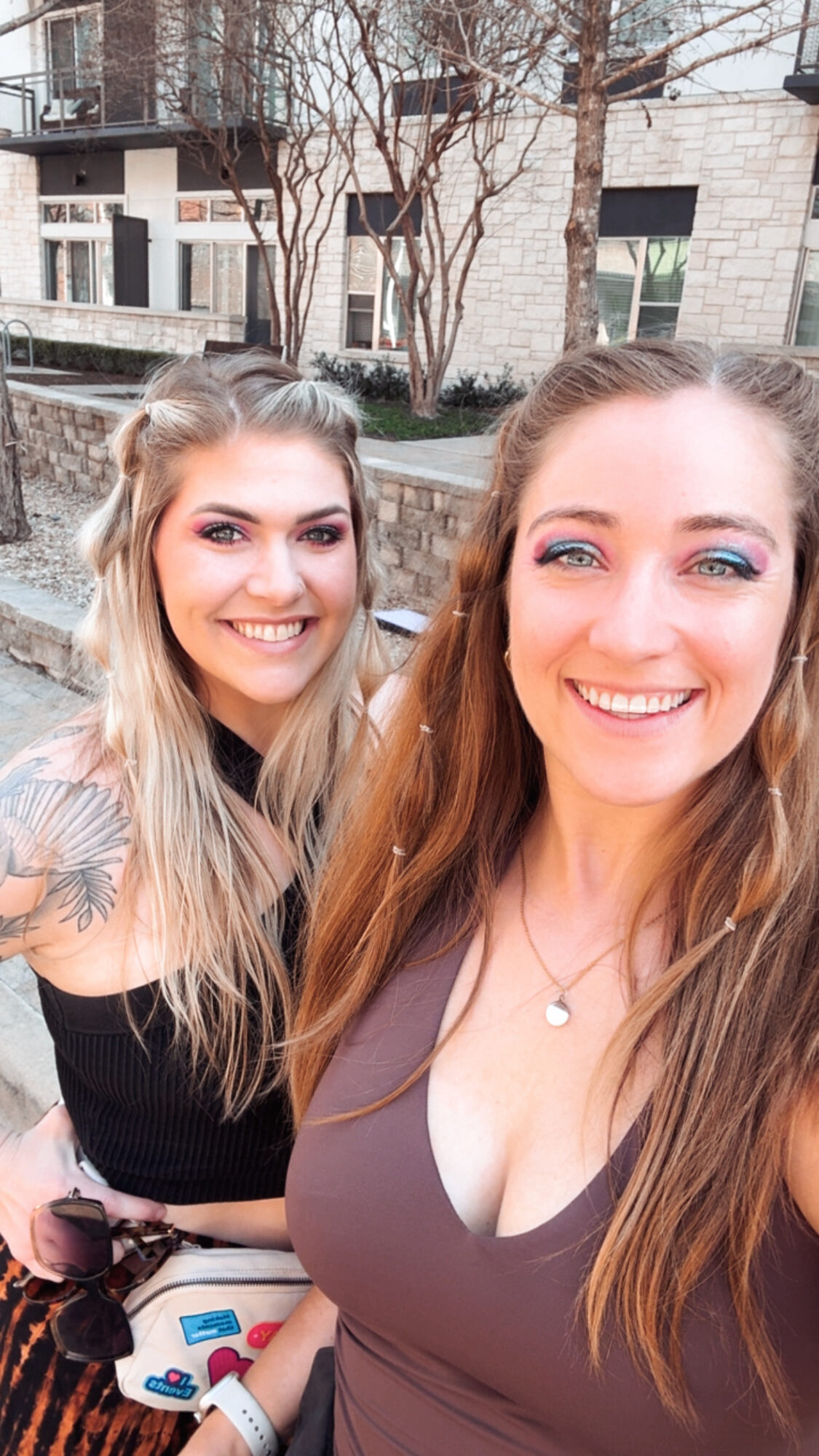 Two people pose for a selfie outdoors in front of a stone building and leafless trees.