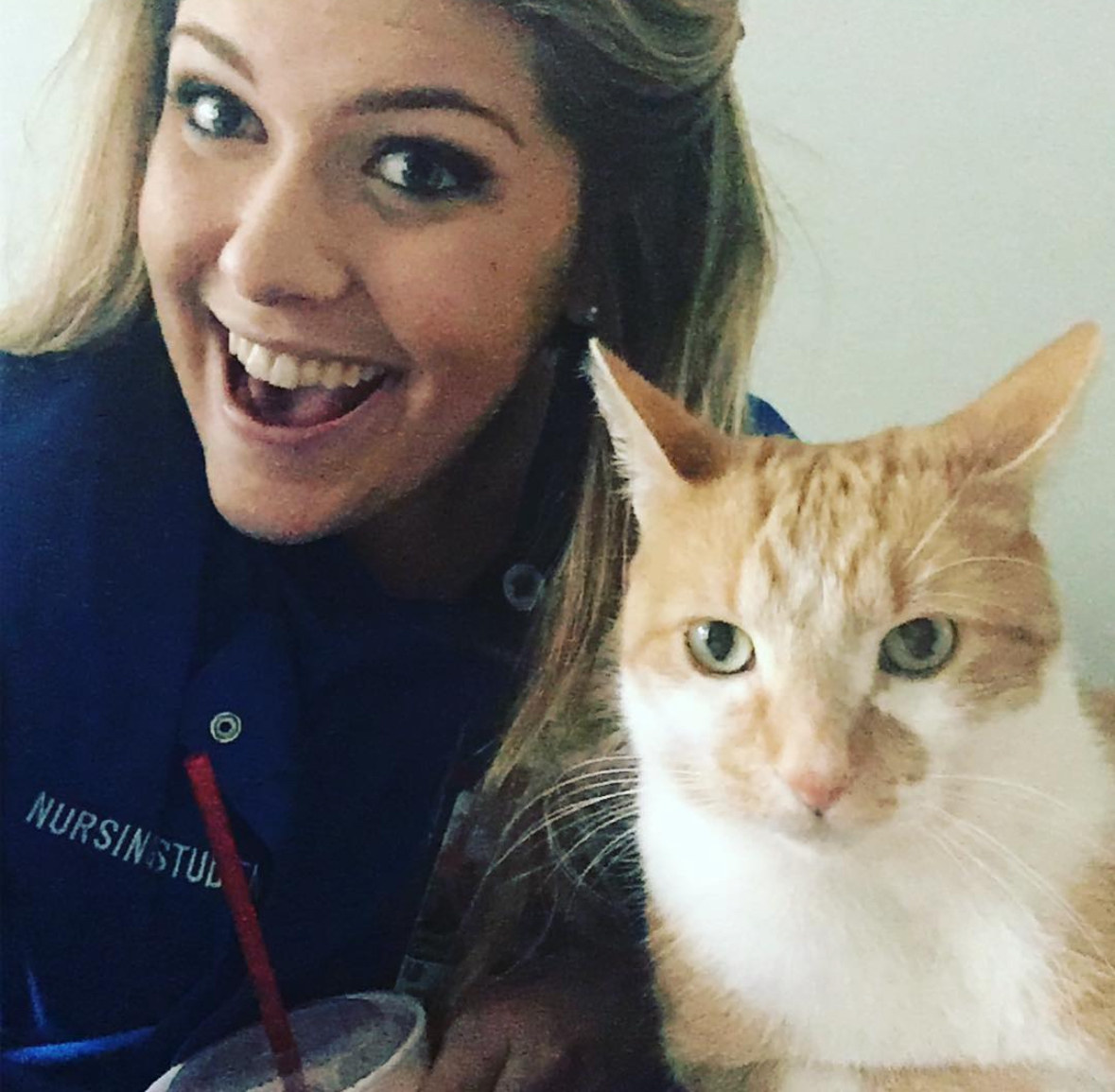 A smiling person in a navy uniform poses beside an orange-and-white cat.
