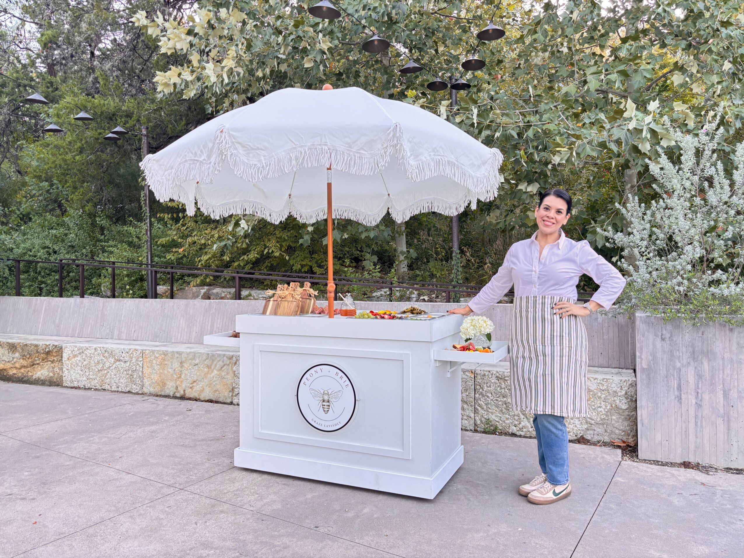 Person standing beside a small cart under a white parasol in an outdoor plaza.
