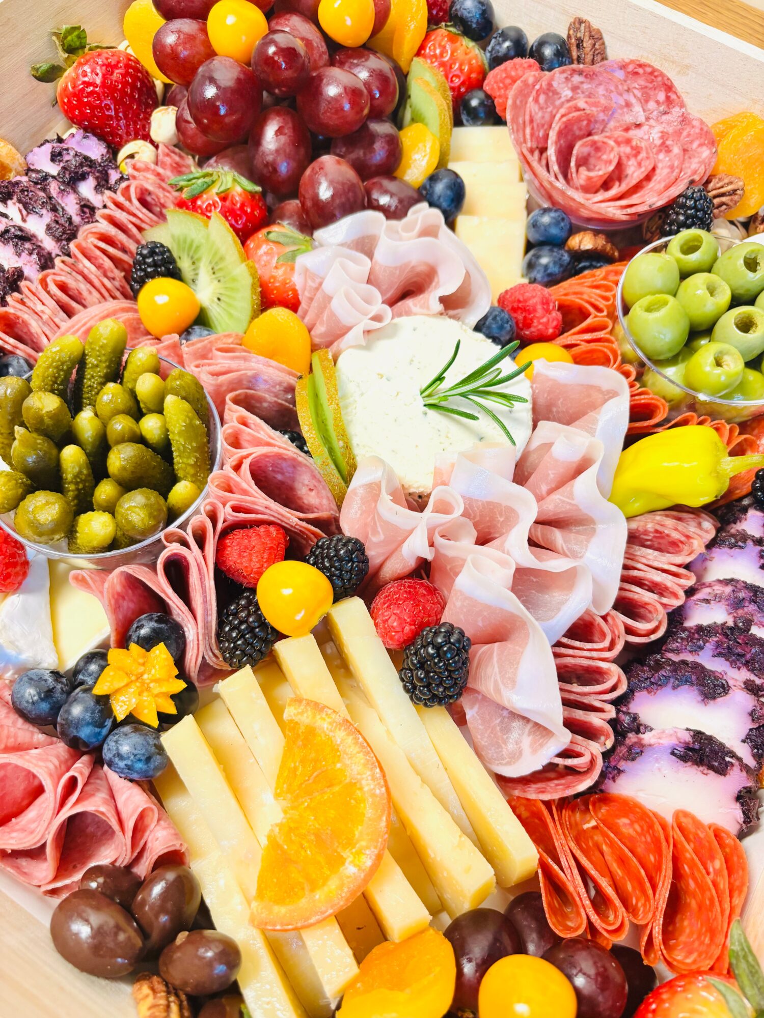 A colorful platter of sliced meats, cheeses, olives, berries, grapes, citrus, and other fruit.