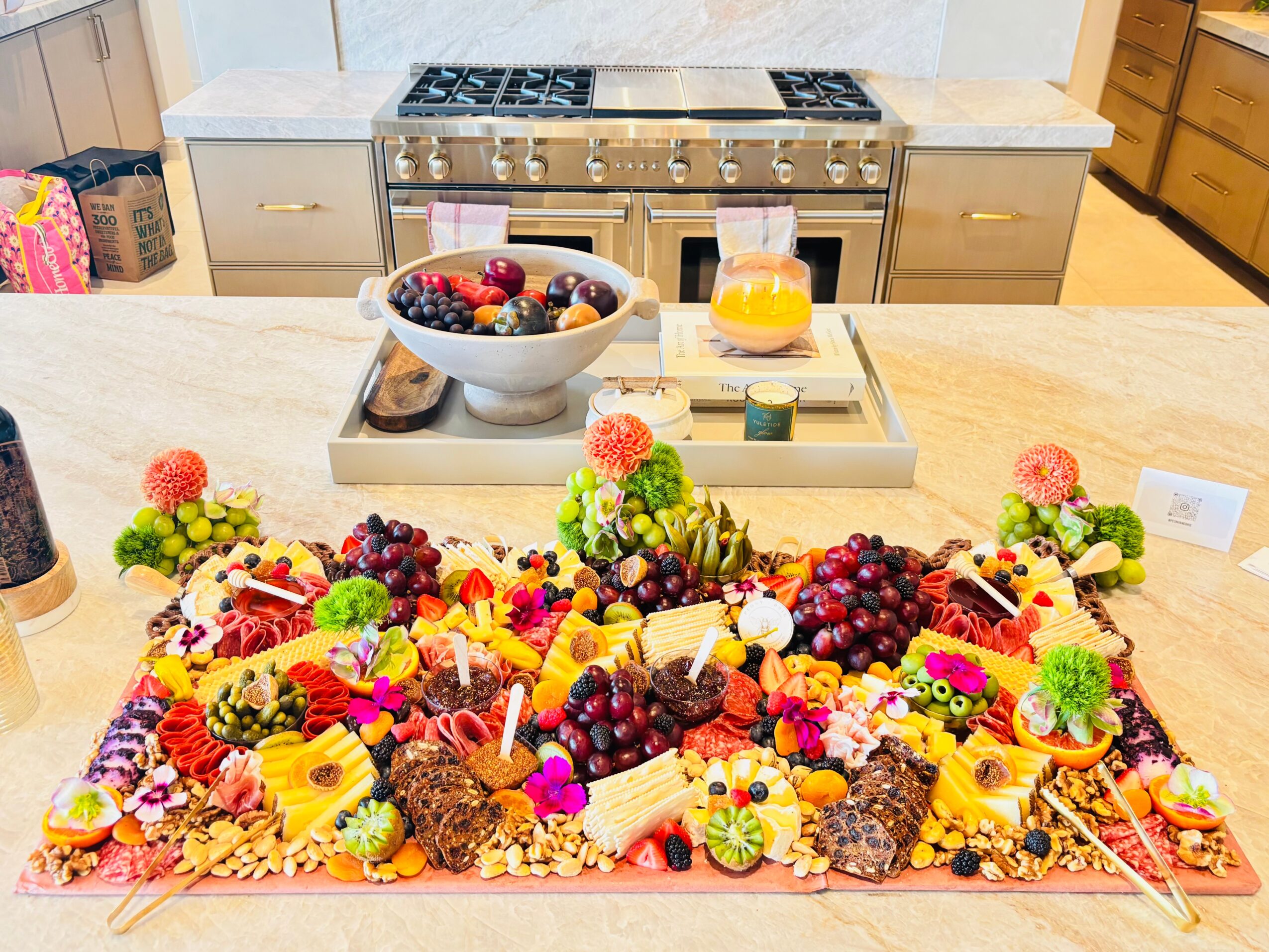 A large fruit and cheese platter arranged on a kitchen island, with a stove and bowls behind it.