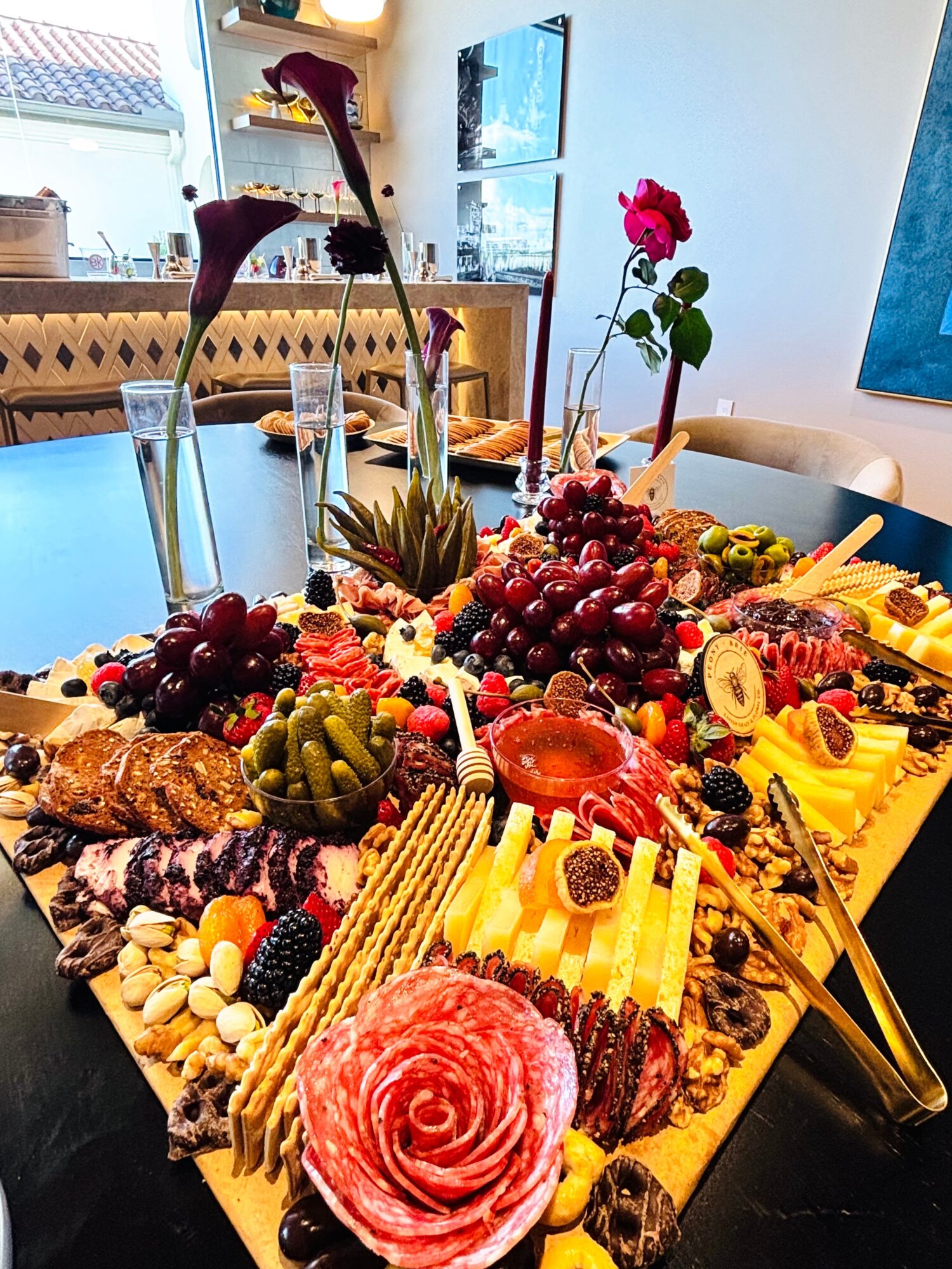 A large charcuterie spread with cheeses, meats, fruit, olives, and flowers on a table.