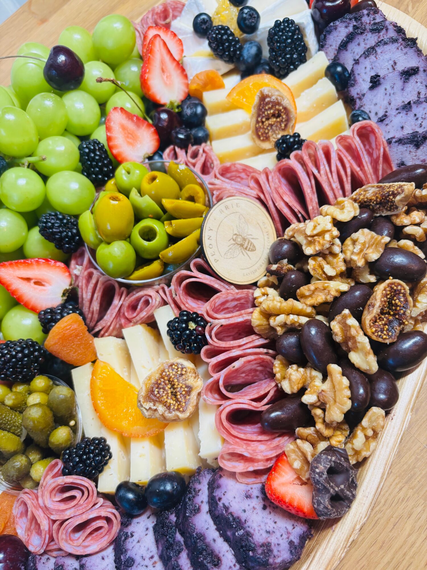 A platter arranged with sliced meats, cheeses, olives, berries, grapes, figs, and walnuts.