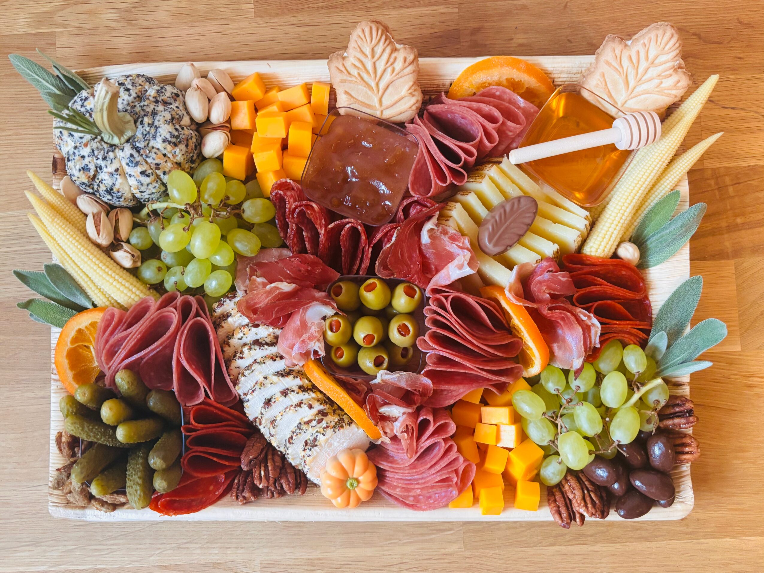 A wooden board arranged with sliced meats, cheeses, grapes, olives, nuts, fruit, and crackers.