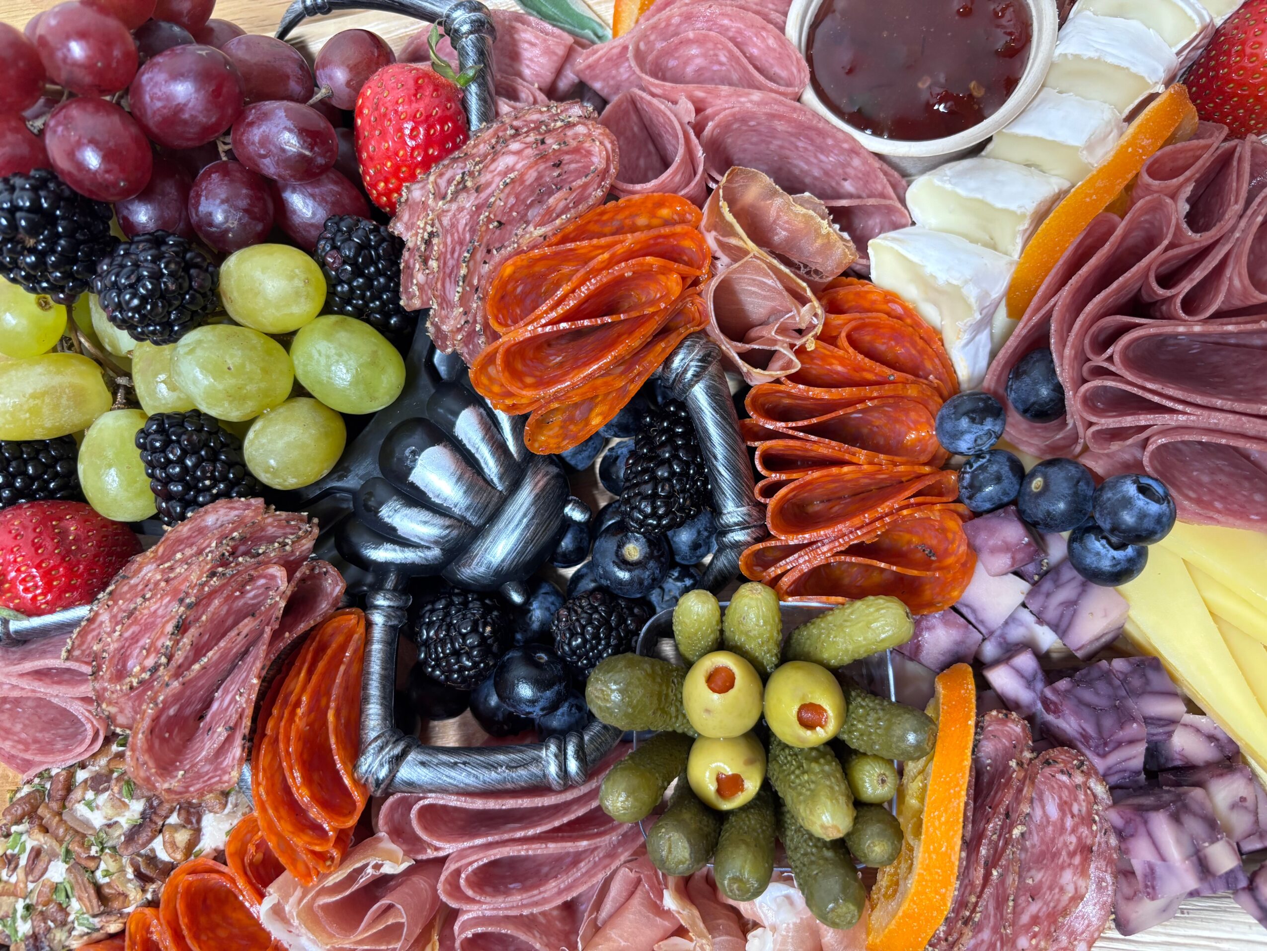A platter arranged with sliced meats, grapes, berries, olives, cheese, and strawberries.