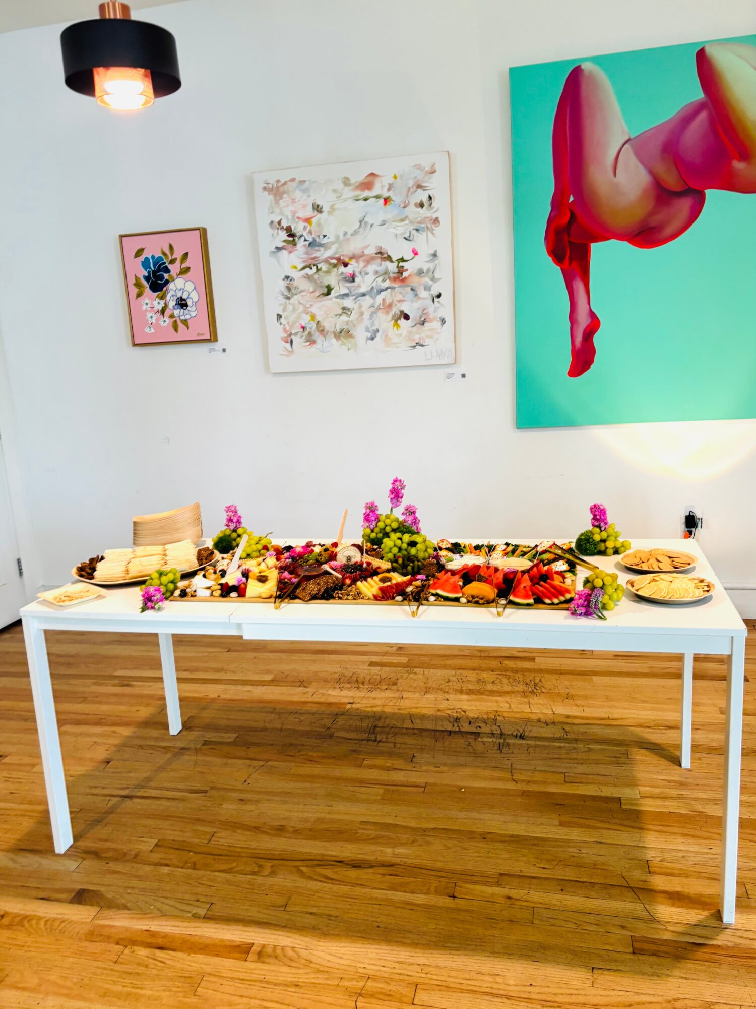 A long white table covered with flowers, food, and dishes beneath colorful wall art.