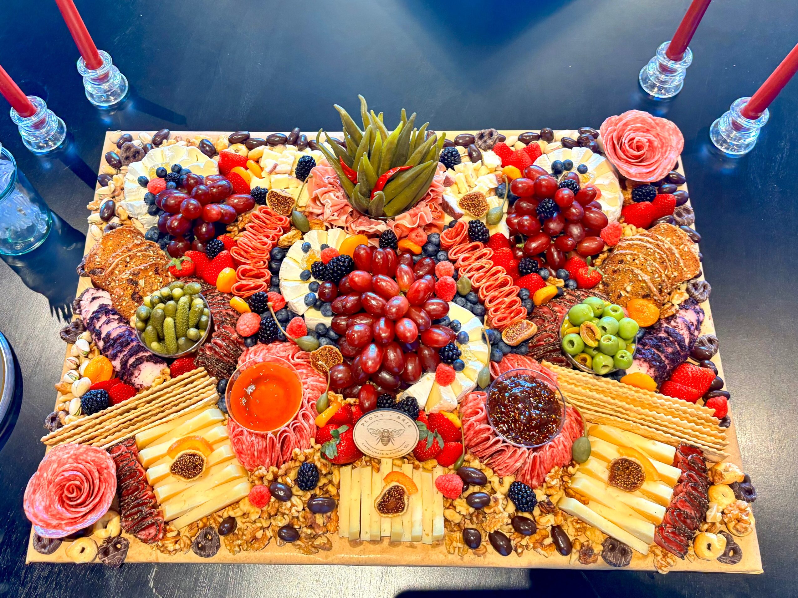 A large rectangular platter filled with grapes, berries, sliced fruit, cheeses, crackers, and decorative garnishes.